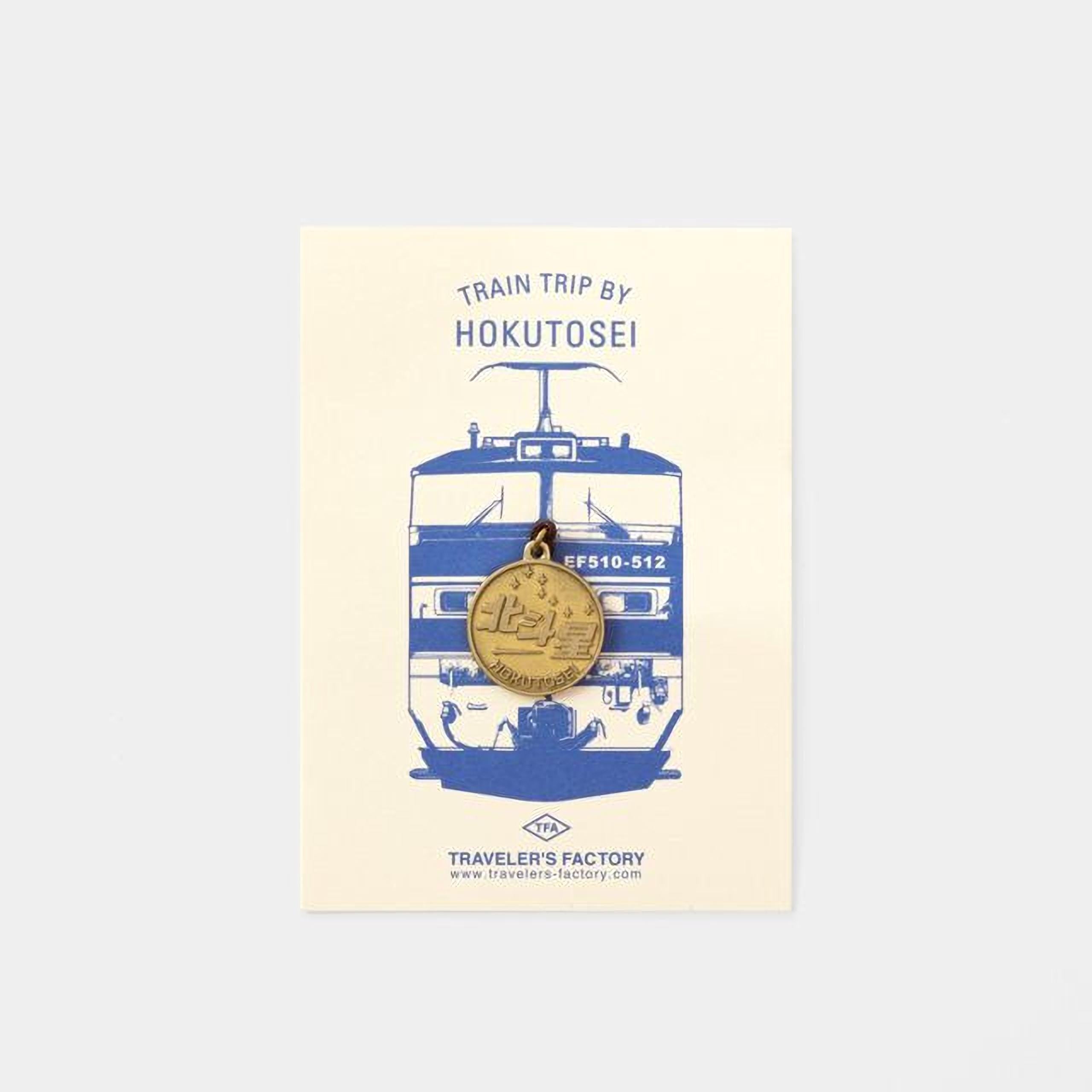 The image is a promotional poster for a train trip by Hokutosei, featuring a blue and white illustration of a train and a gold-colored charm with Japanese characters.