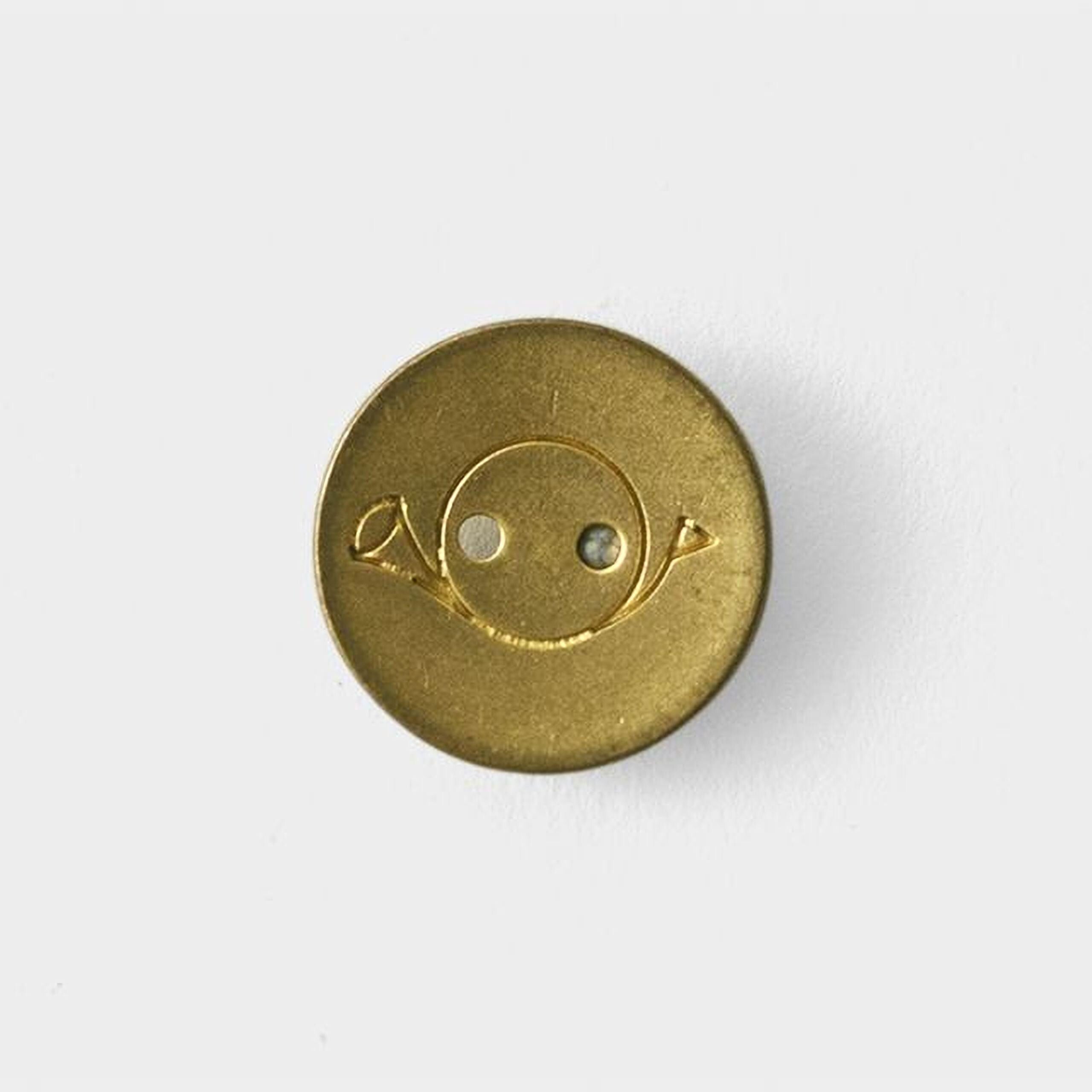 A gold-colored button with a face-like symbol on it.