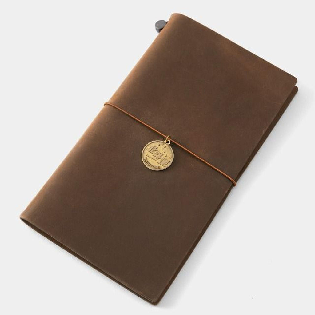 A brown leather-bound notebook with a gold-colored charm attached to the cover.