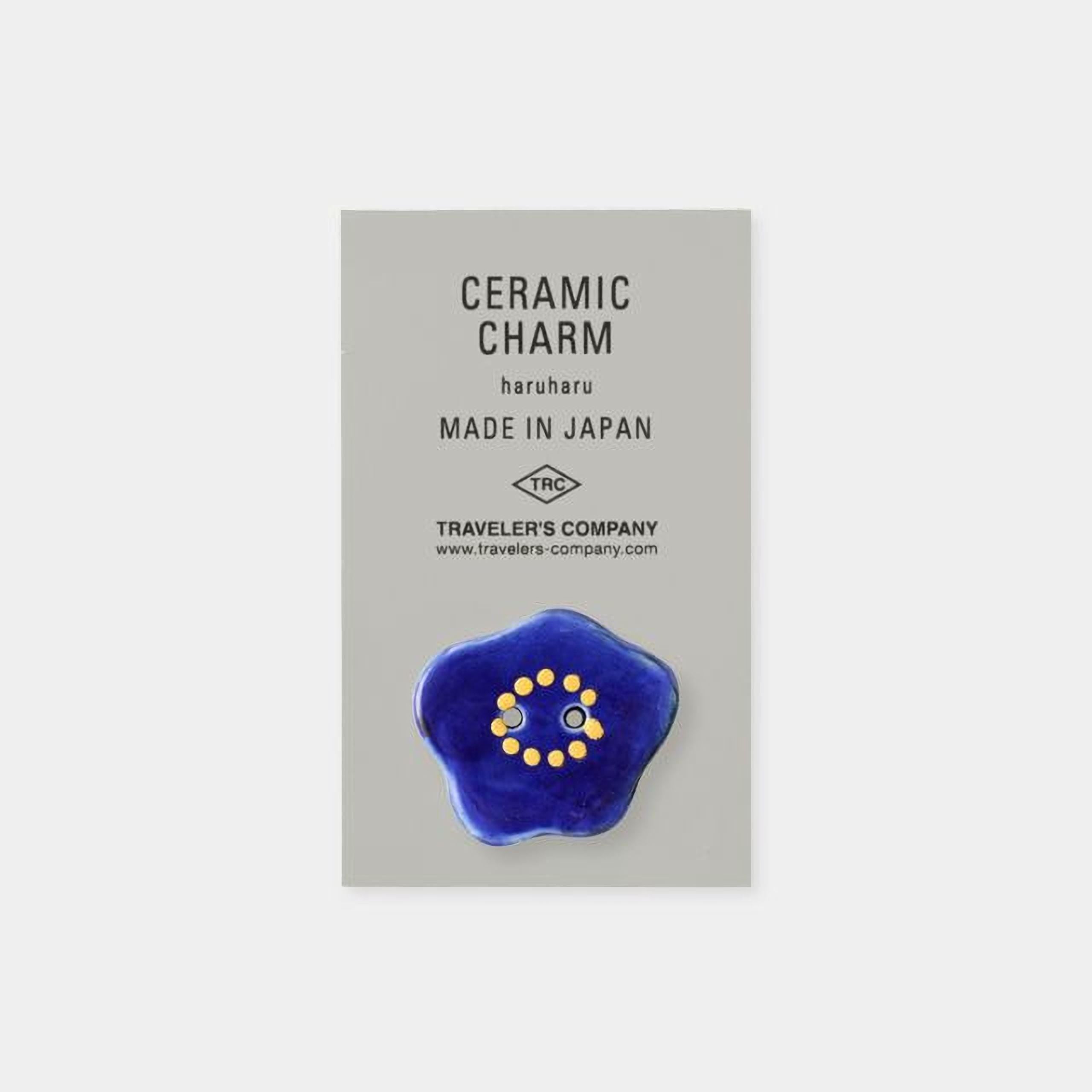The image is a product advertisement for ceramic charms, specifically the "Ceramic Charm Haruharu Made in Japan". The product is described as a "Ceramic Charm" and is made in Japan. The ad also mentions that the product is from the "Traveler's Company" and includes a website address for further information.