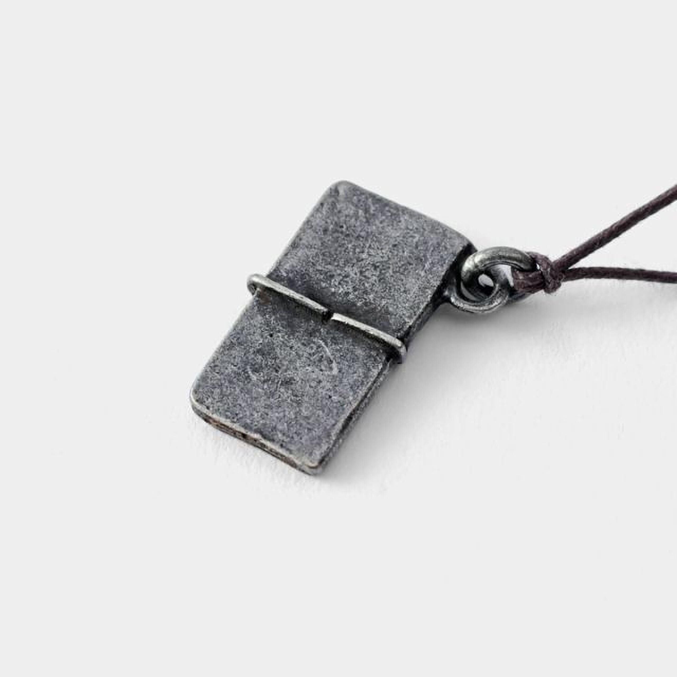 A small, rectangular metal pendant with a textured surface, attached to a cord.