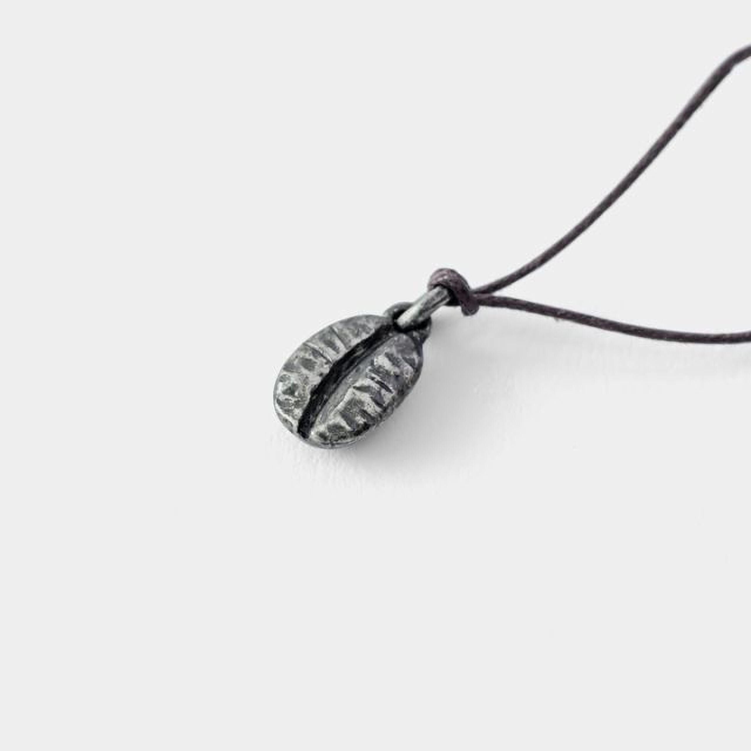 A silver pendant in the shape of a coffee bean is shown against a white background.