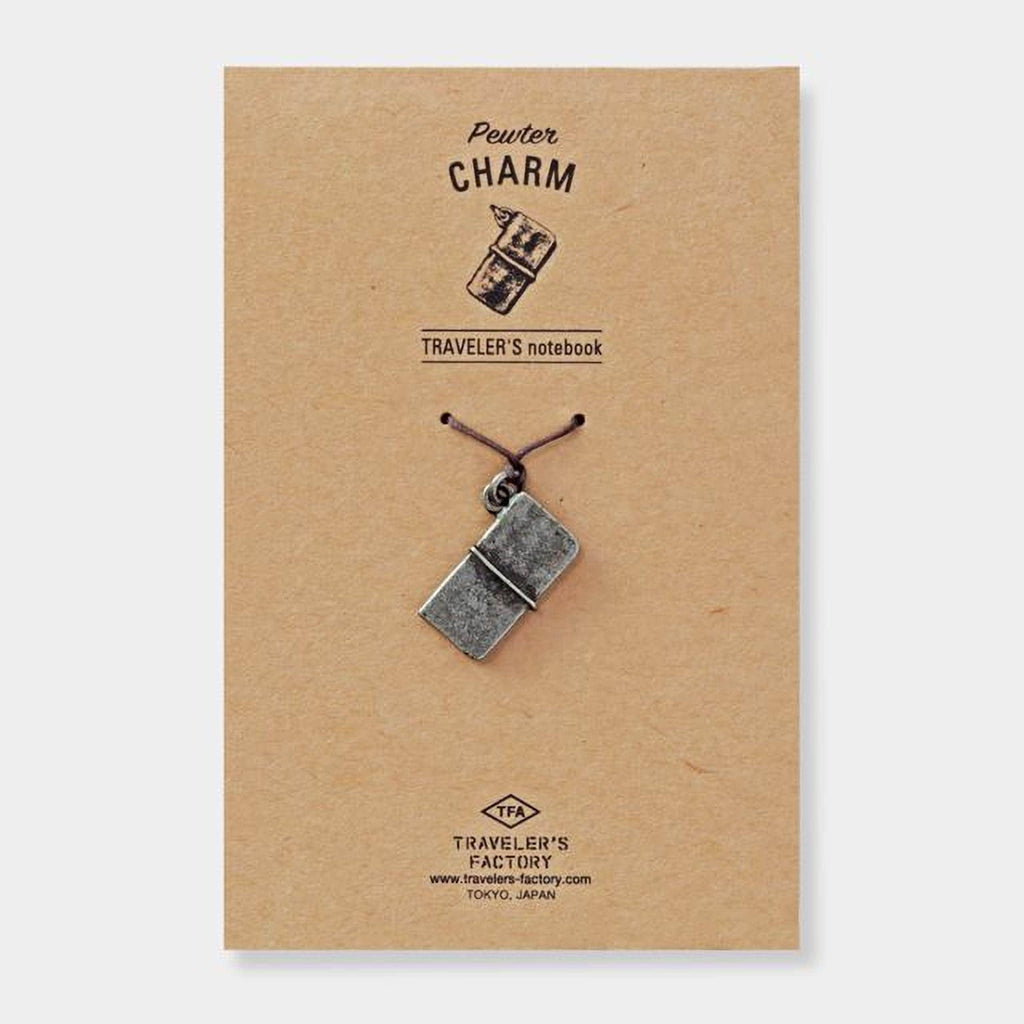 A pewter charm in the shape of a book is attached to a brown paper background, with the text "Pewter Charm" and "TRAVELER'S notebook" printed on it.