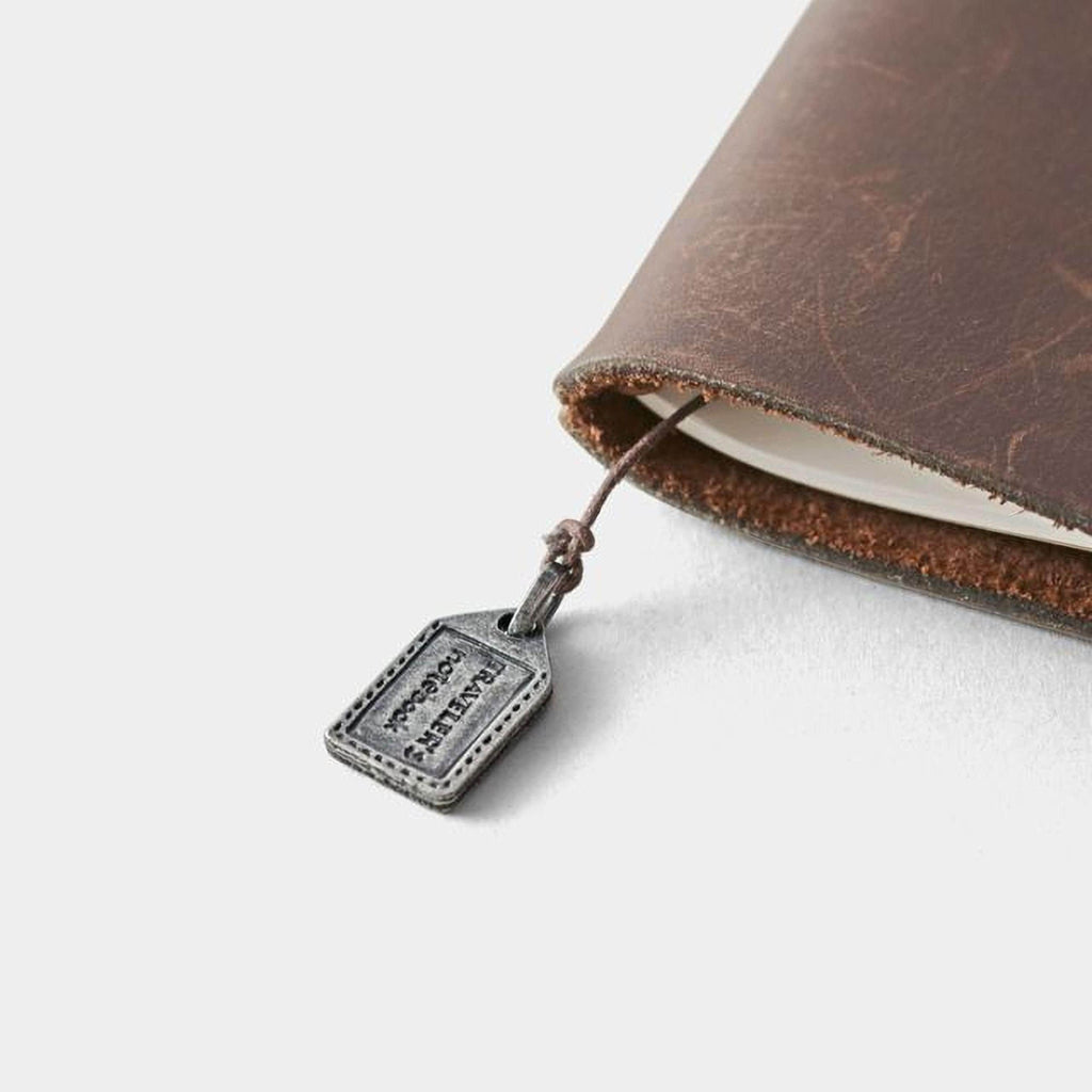 A small metal tag attached to a leather-bound notebook or journal.