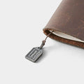 A small metal tag attached to a leather-bound notebook or journal.