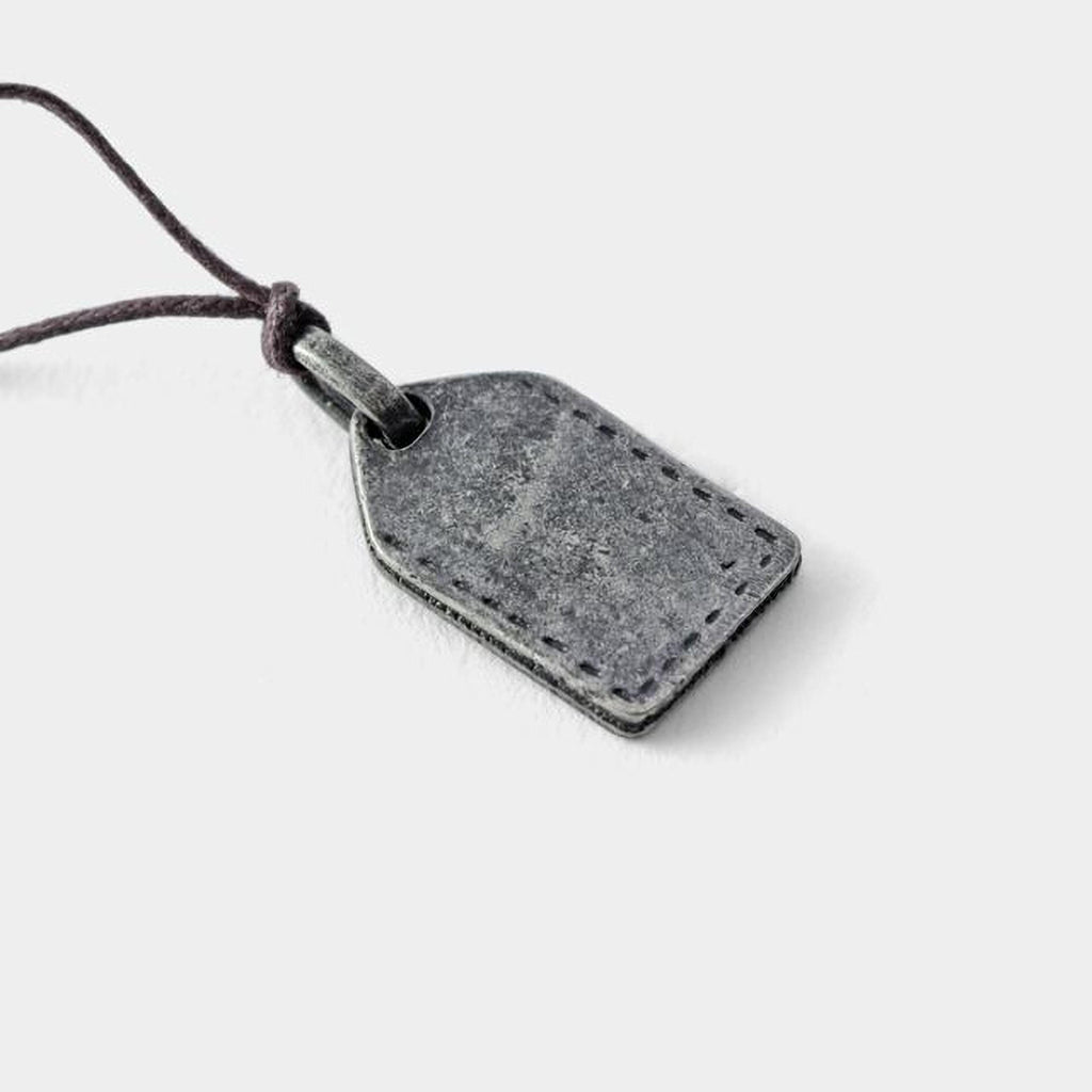 A gray metal tag with a cord attached, resting on a plain white background.