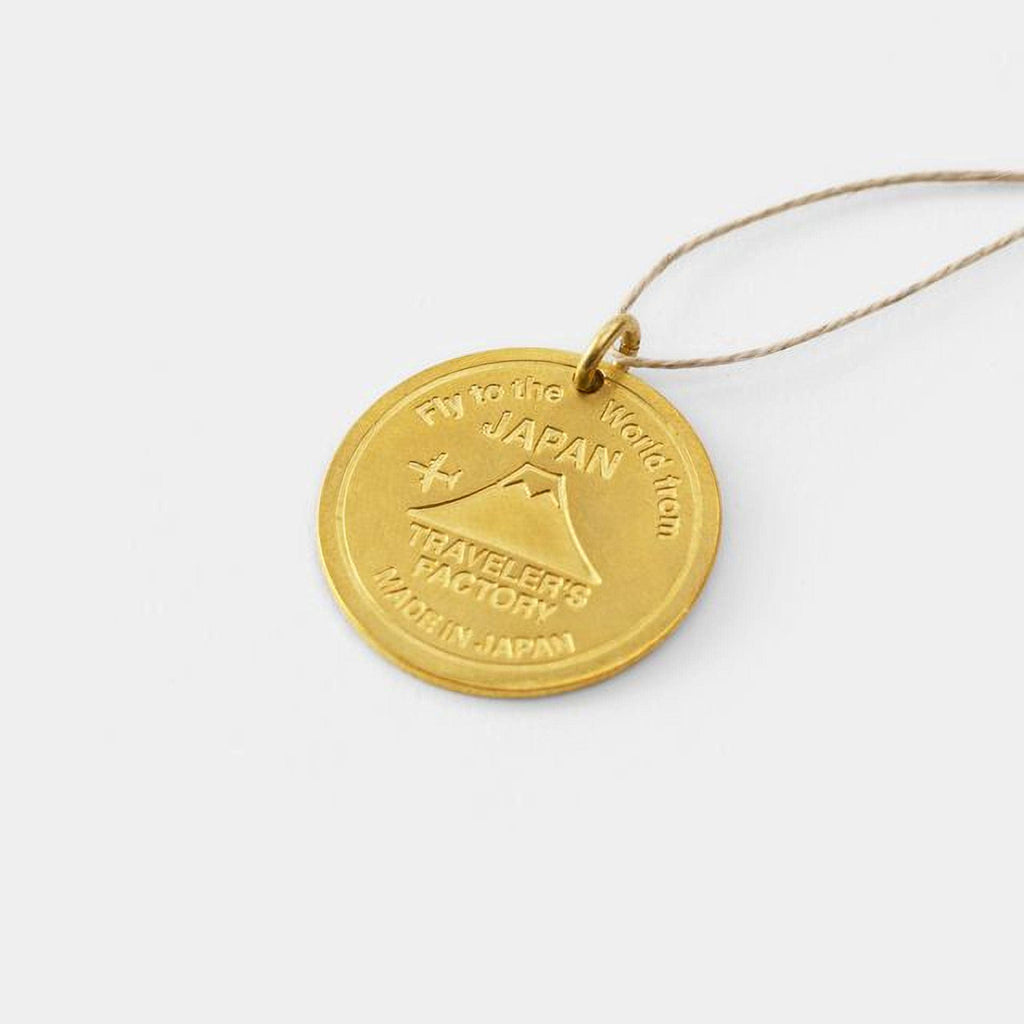 A gold-colored pendant with the text "Fly to the World from Japan" engraved on it.