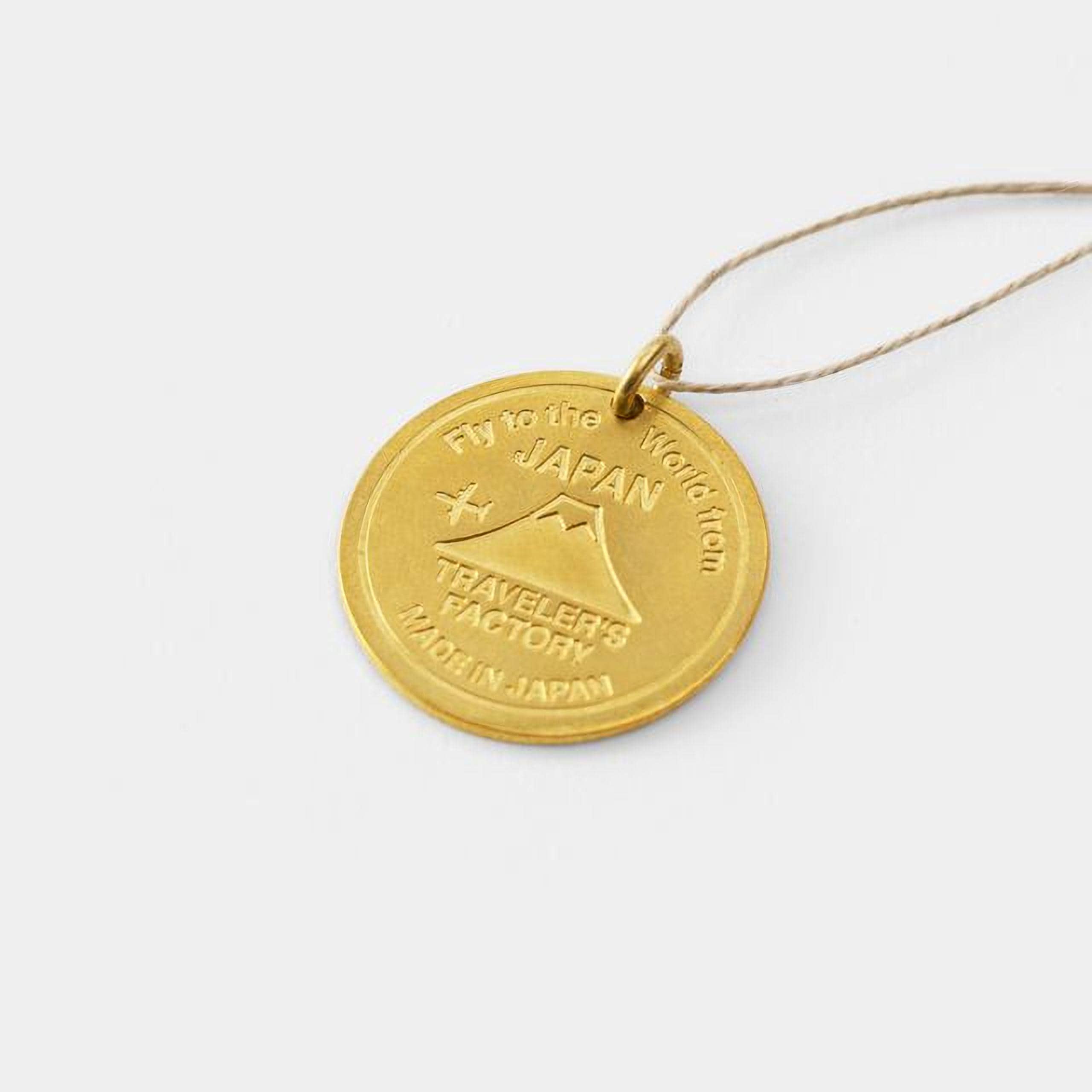 A gold-colored pendant with the text "Fly to the World from Japan" engraved on it.