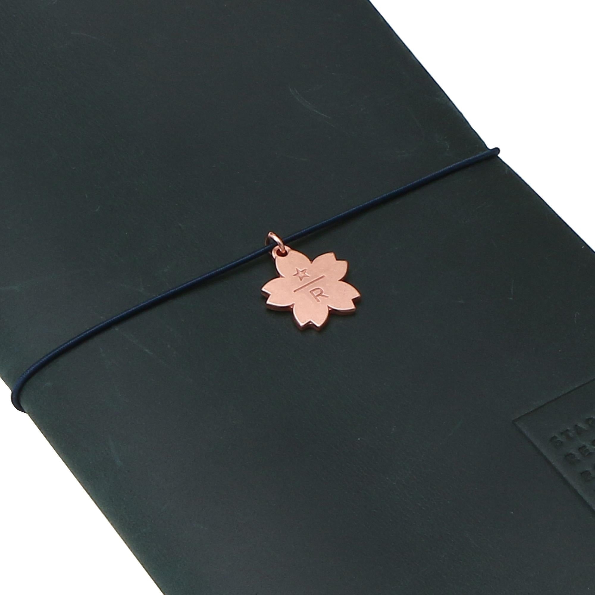 A black leather-bound notebook with a copper-colored charm featuring a flower-like design attached to it.