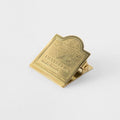 A gold-colored metal clip with embossed text and an image of a plane on it.