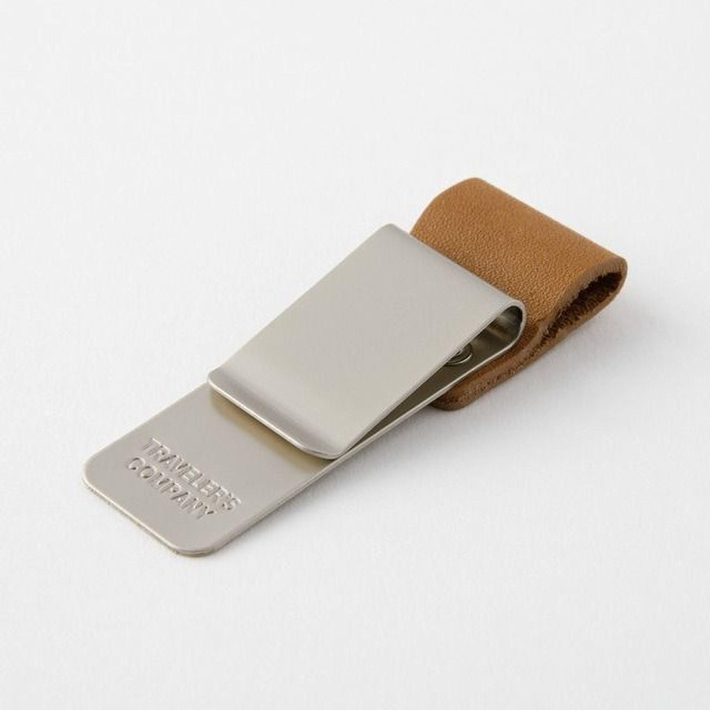 A silver metal money clip with a leather pouch attached to it, resting on a white surface.