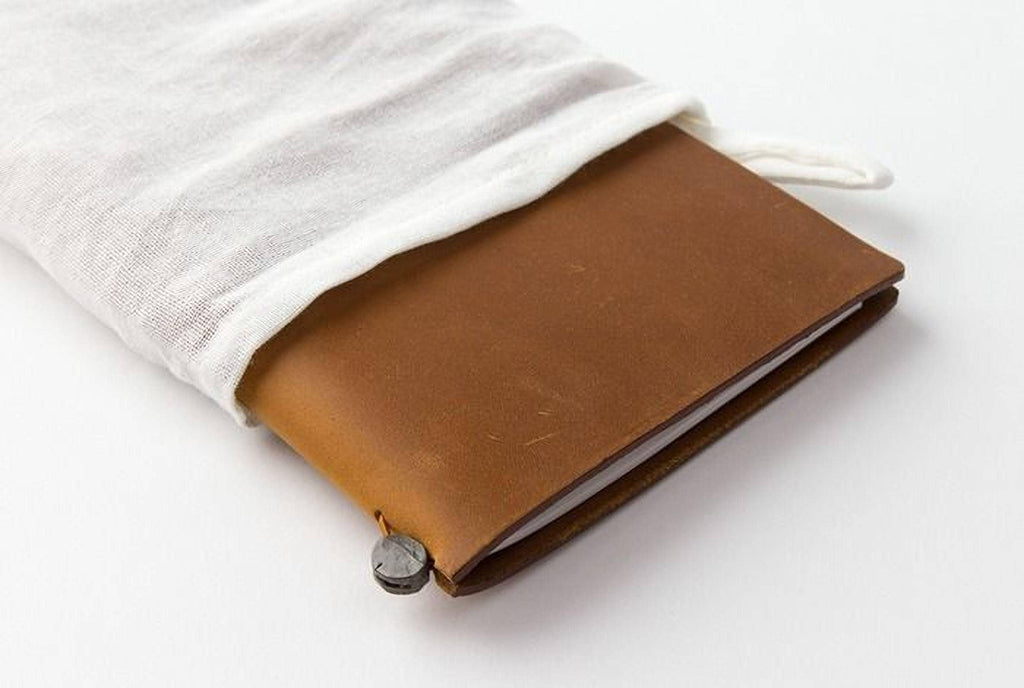A brown leather-bound notebook with a white cloth bag partially covering it, placed on a white surface.