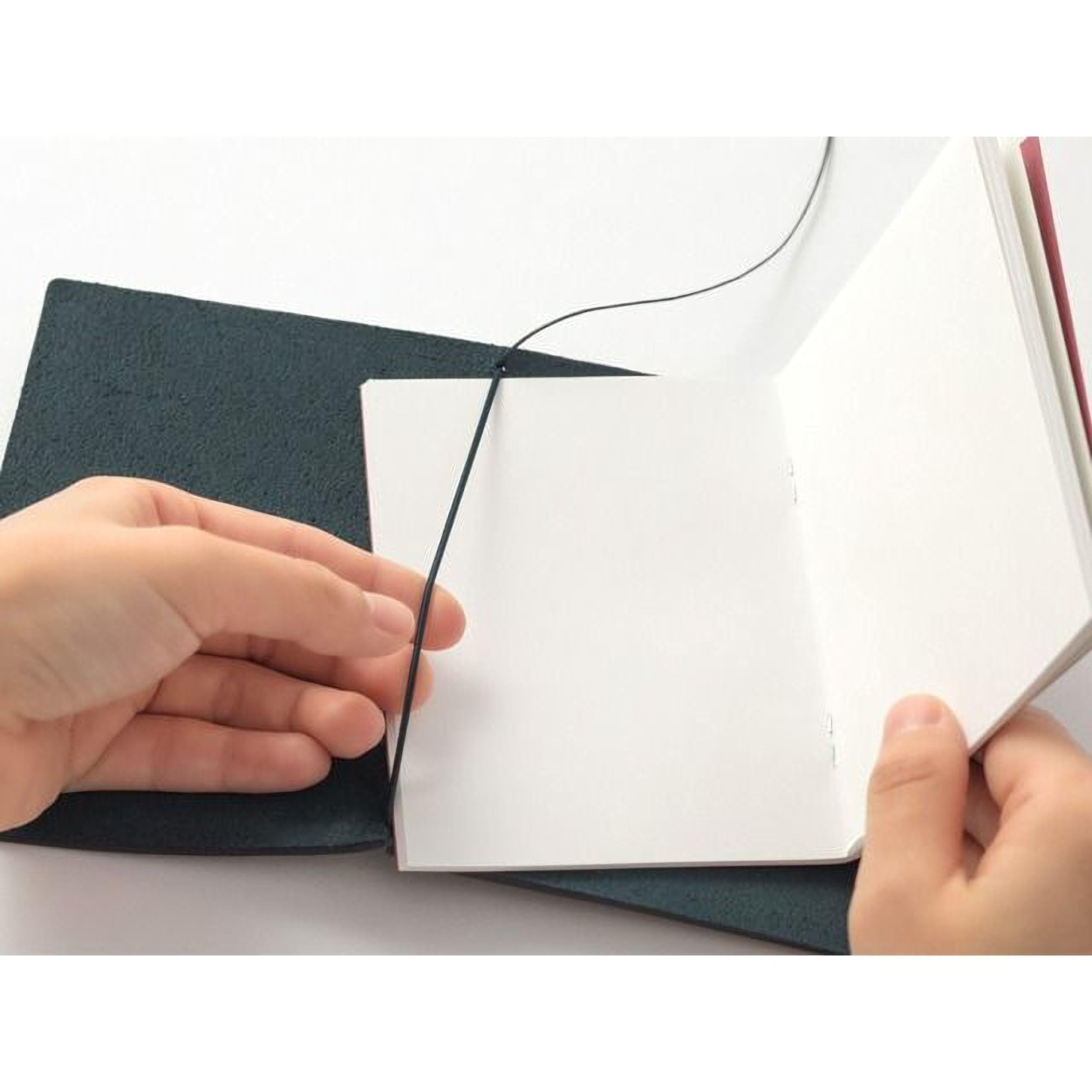 A person's hands are holding open a black notebook with a blank page inside, against a white background.