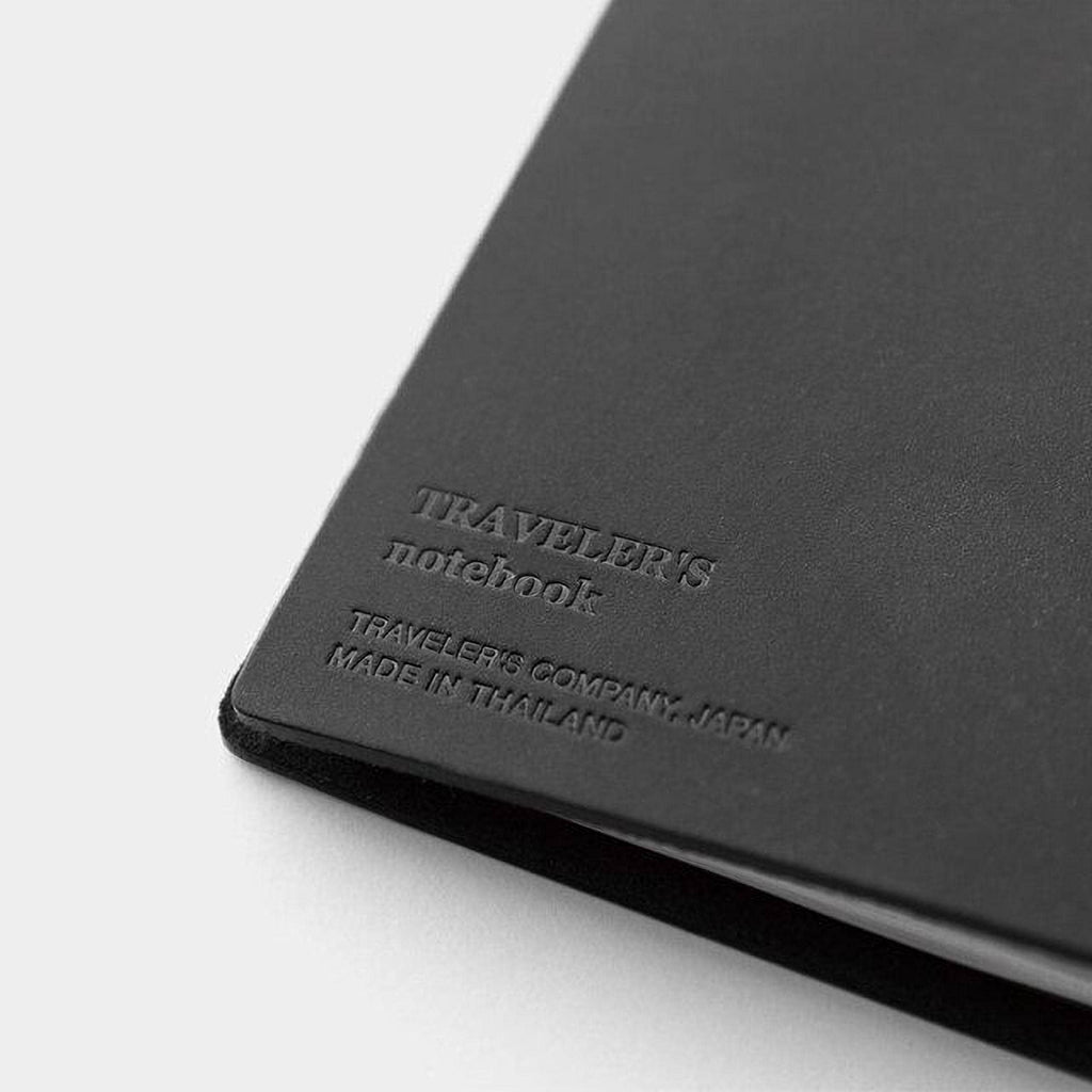 A black notebook with embossed text that reads "TRAVELER'S notebook" and "TRAVELER'S COMPANY, JAPAN MADE IN THAILAND".