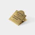 A gold-colored metal clip or binder with the text "TRAVELER'S COMPANY JAPAN TRAVELER'S NOTEBOOK MADE IN JAPAN" printed on it.