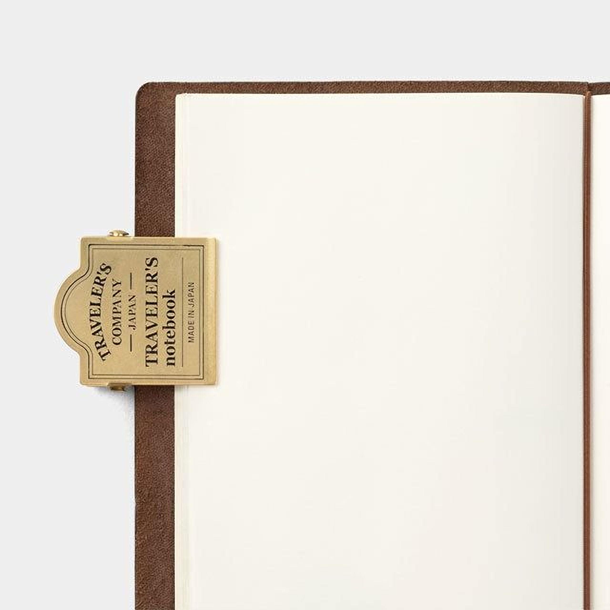 a brown leather-bound notebook with a gold metal clip attached to the top left corner.