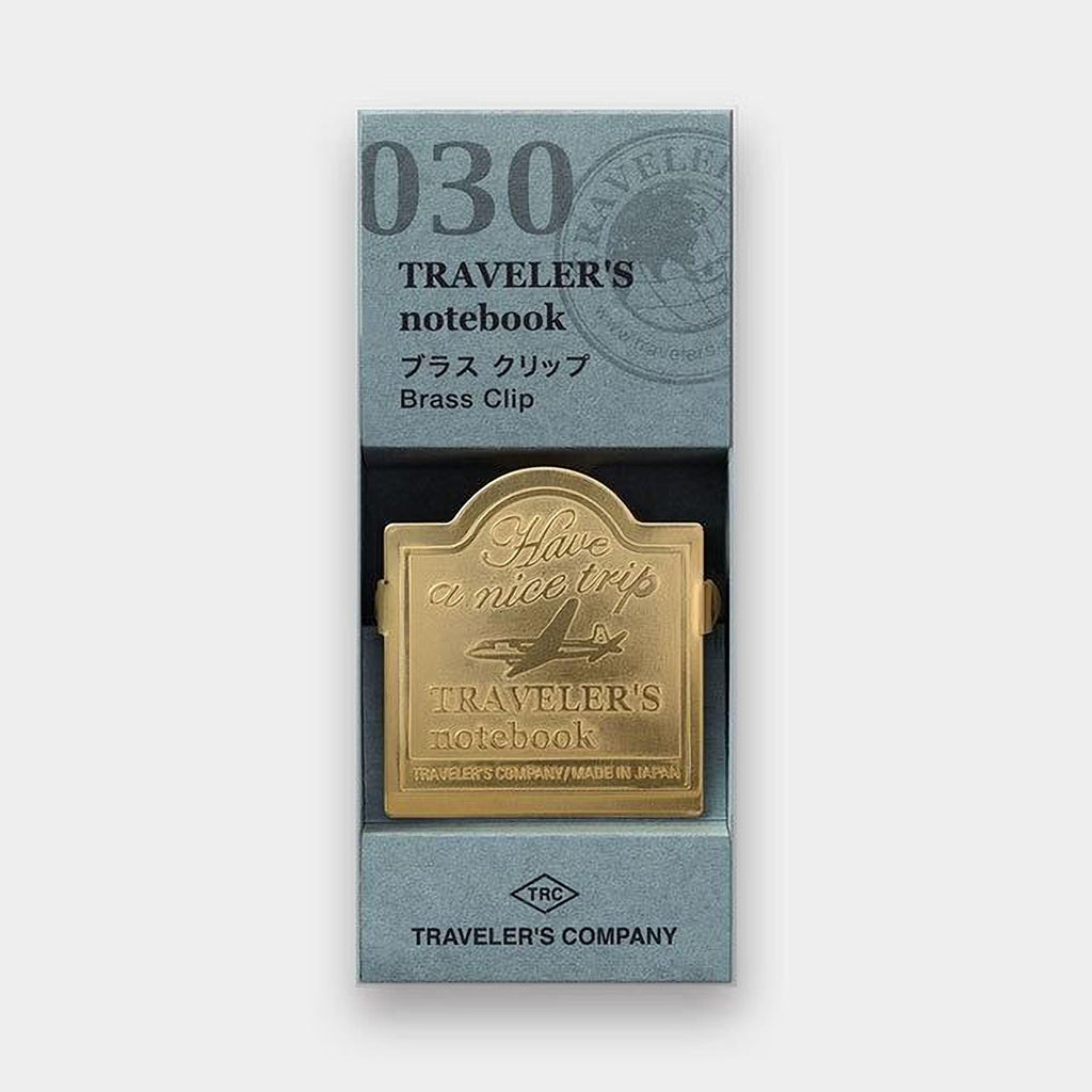 A gold-colored brass clip with the text "Traveler's notebook" printed on it, placed inside a box with a gray background.