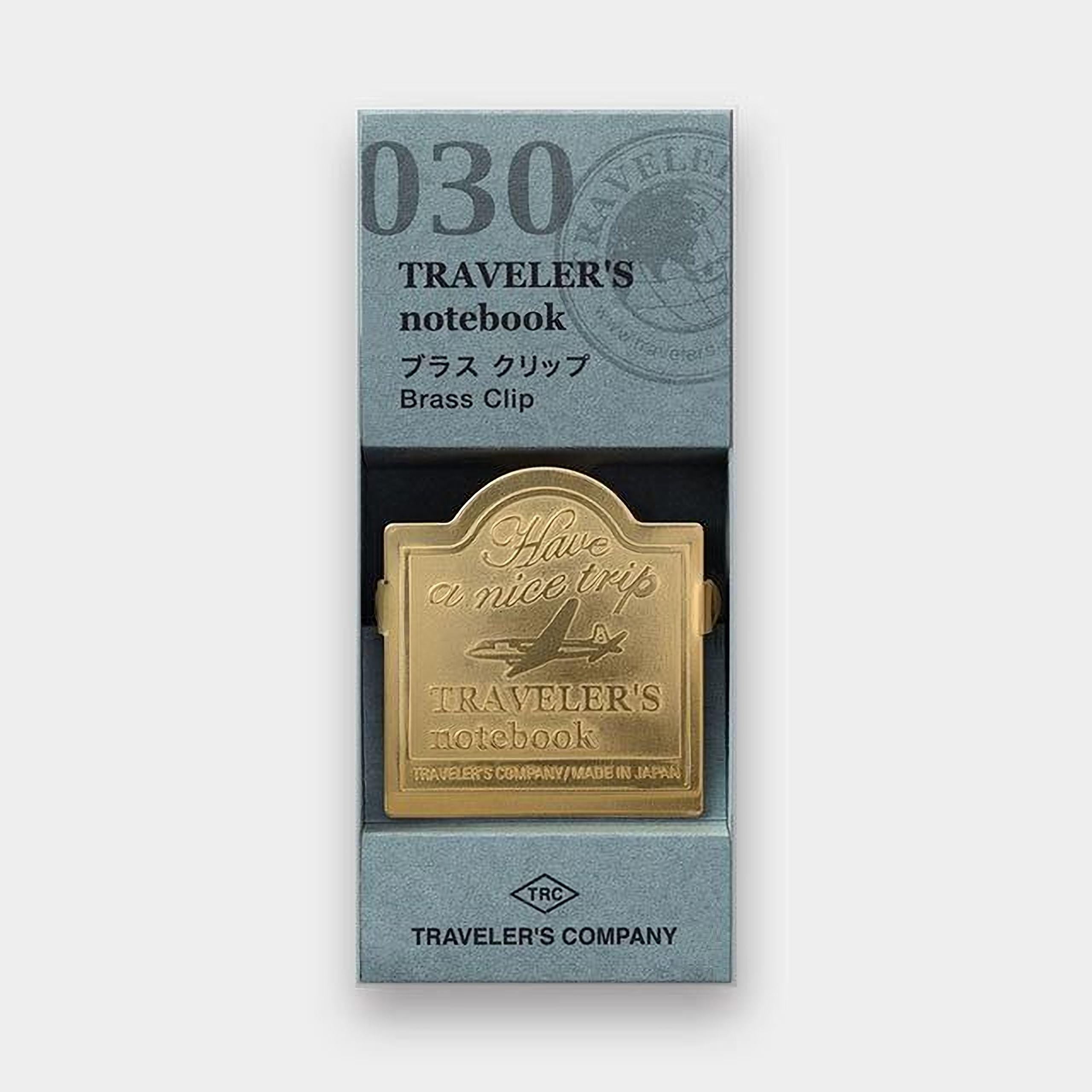 A gold-colored brass clip with the text "Traveler's notebook" printed on it, placed inside a box with a gray background.