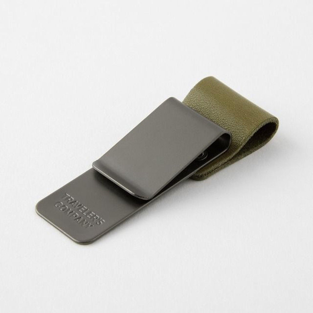 A metal clip with a leather strap attached to it, resting on a white surface.