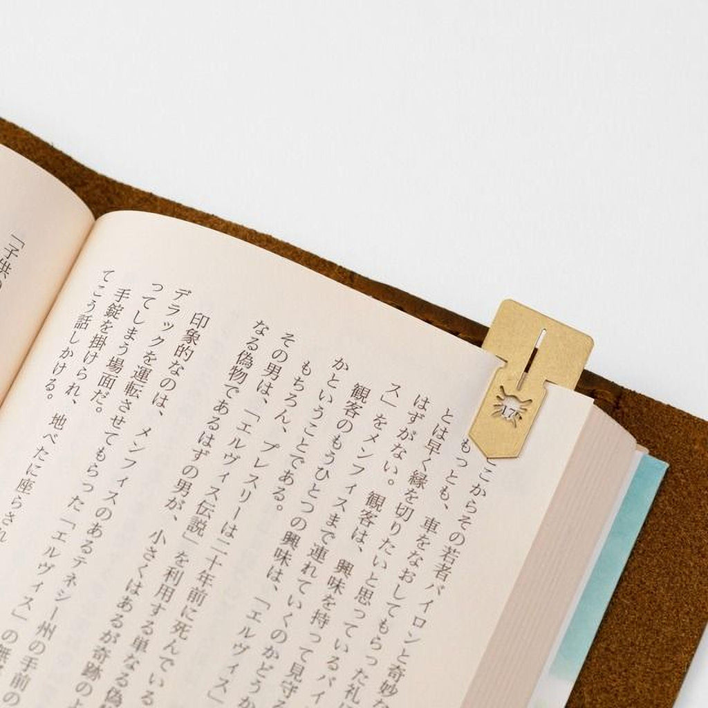 an open book with Japanese text on the pages, and a gold-colored metal bookmark or clip resting on the right page.