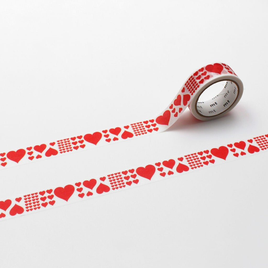 A roll of red heart-shaped tape is lying on a white surface, with a repeating pattern of red hearts on the tape.