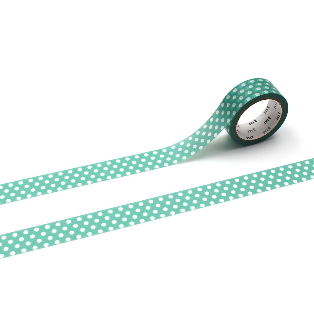 A roll of green and white polka dot tape is lying on a white surface, with the tape partially unspooled.