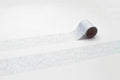 A roll of patterned tape is lying on a white surface, with a repeating pattern of white and gray designs.