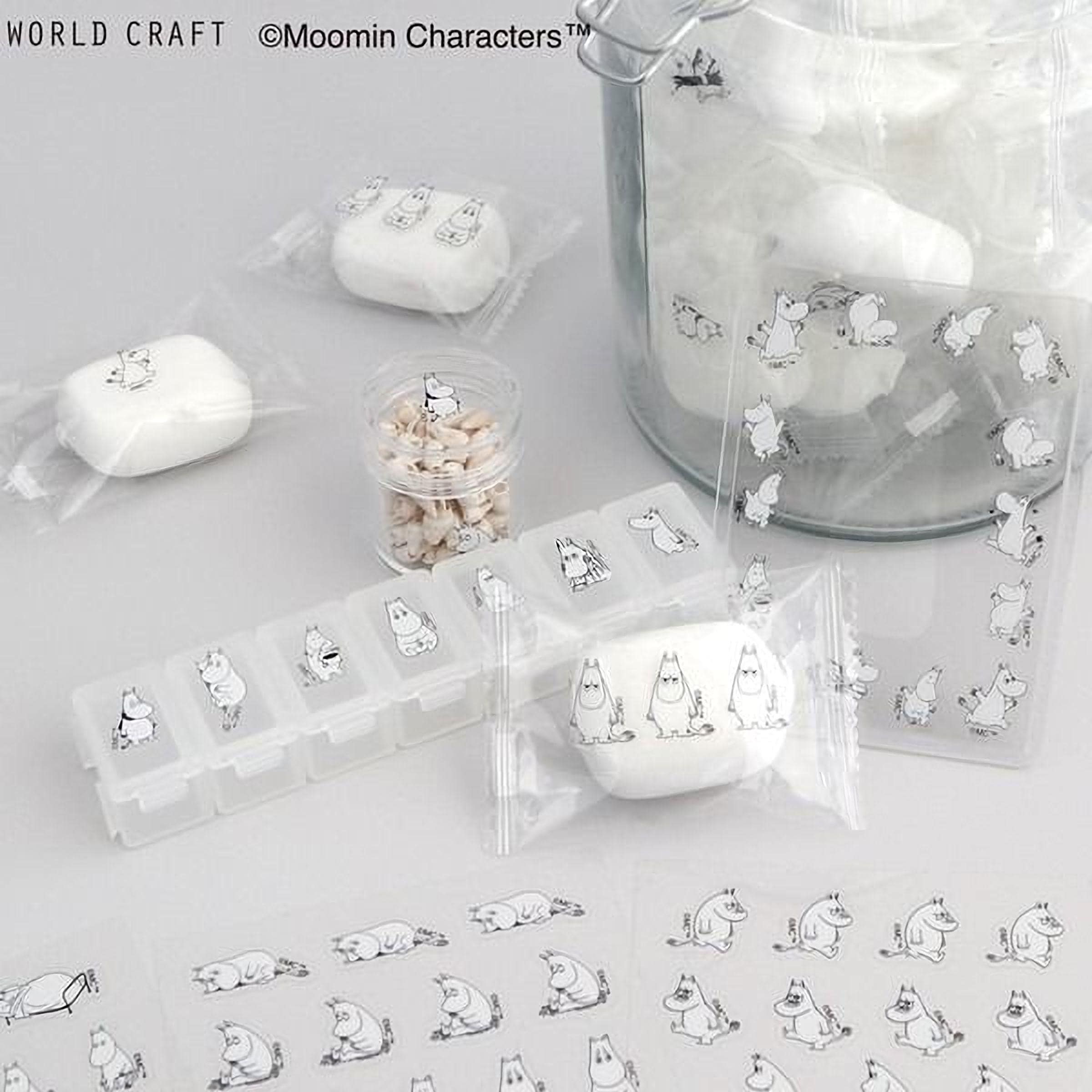 various items related to the Moomin character, including a glass jar filled with white objects, a pill organizer, and several small white objects. The items are arranged on a white surface, with some of them wrapped in clear plastic.