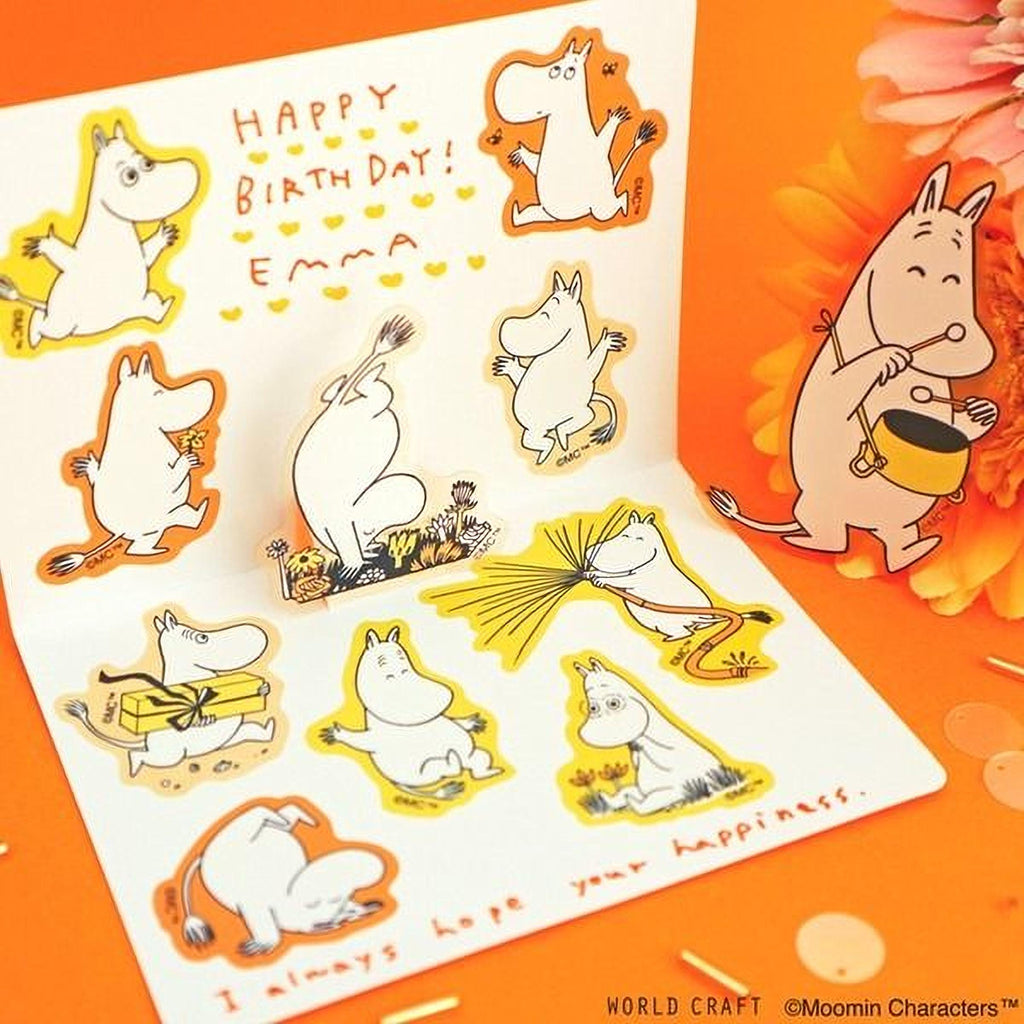 The image is a birthday card featuring illustrations of Moomin characters, including Moomin and Moomin's friends, along with a message and a small illustration of Moomin holding a yellow bucket.