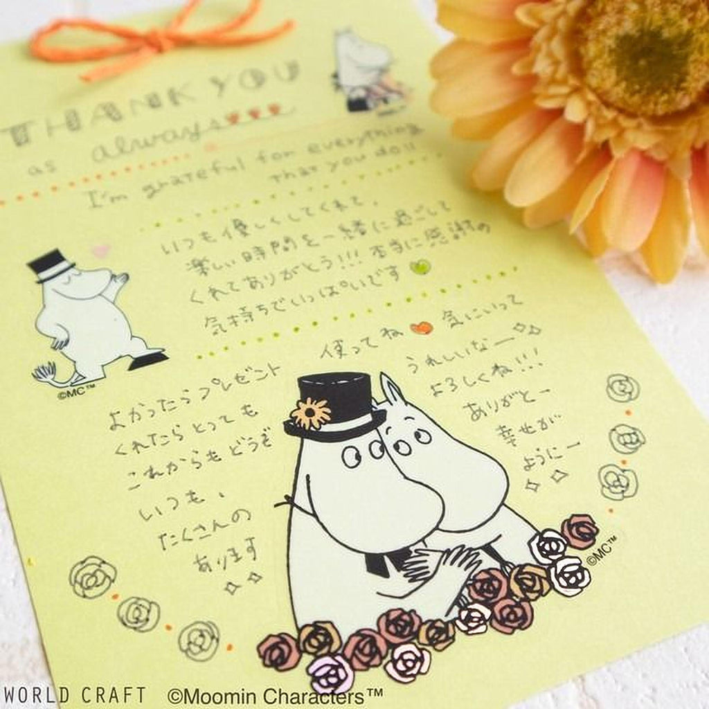 A yellow card with a handwritten message and illustrations of Moomin characters, including a character with a hat and a flower, along with a large orange flower in the background.