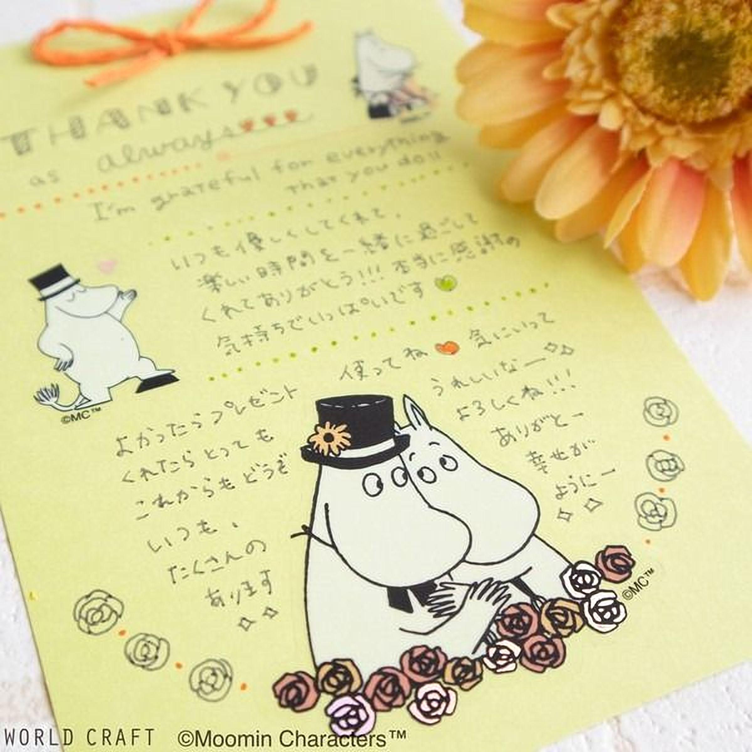 A yellow card with a handwritten message and illustrations of Moomin characters, including a character with a hat and a flower, along with a large orange flower in the background.