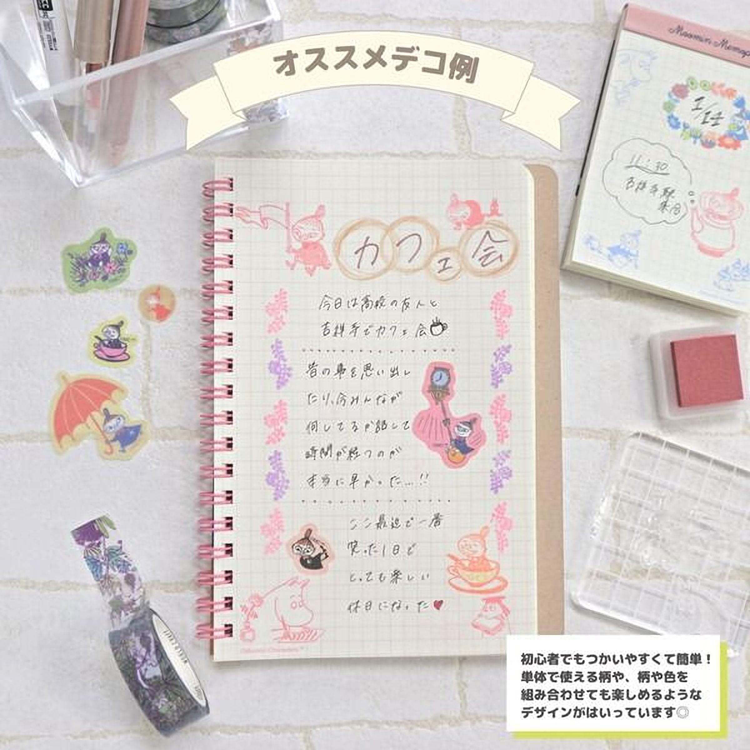 a notebook with Japanese text, a pink and white notebook, and various stationery items such as a red stamp, a clear plastic tray, and a bottle of purple and pink markers.