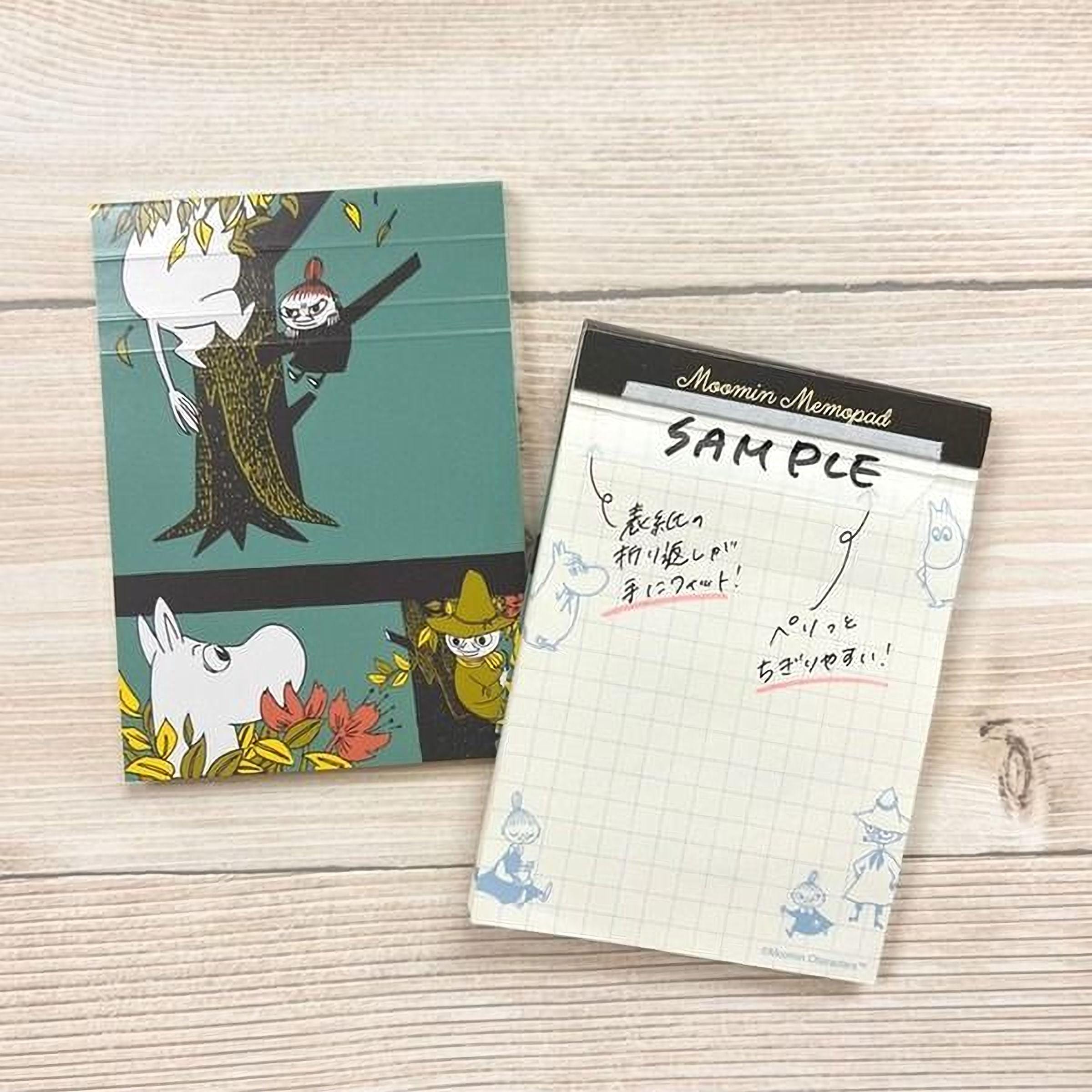 a notebook and a notepad with a grid pattern, both with illustrations of Moomin characters on them. The notebook has a colorful illustration of Moomin characters on the cover, while the notepad has a grid pattern with Moomin characters drawn on it.