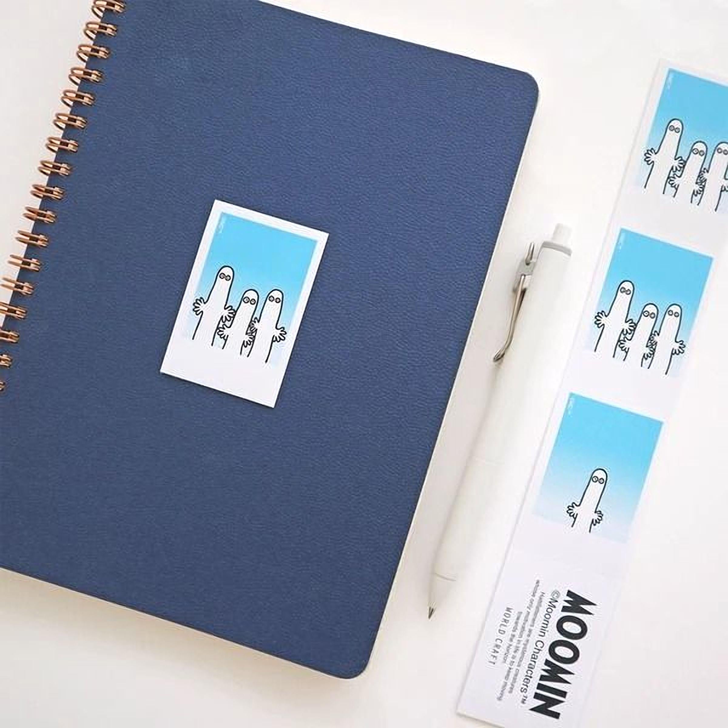 a blue notebook, a white pen, and several stickers with cartoon-style illustrations.