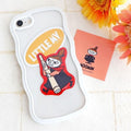 a white phone case with a cartoon character sticker, a pink card with a cartoon character, and some flowers on a white surface.
