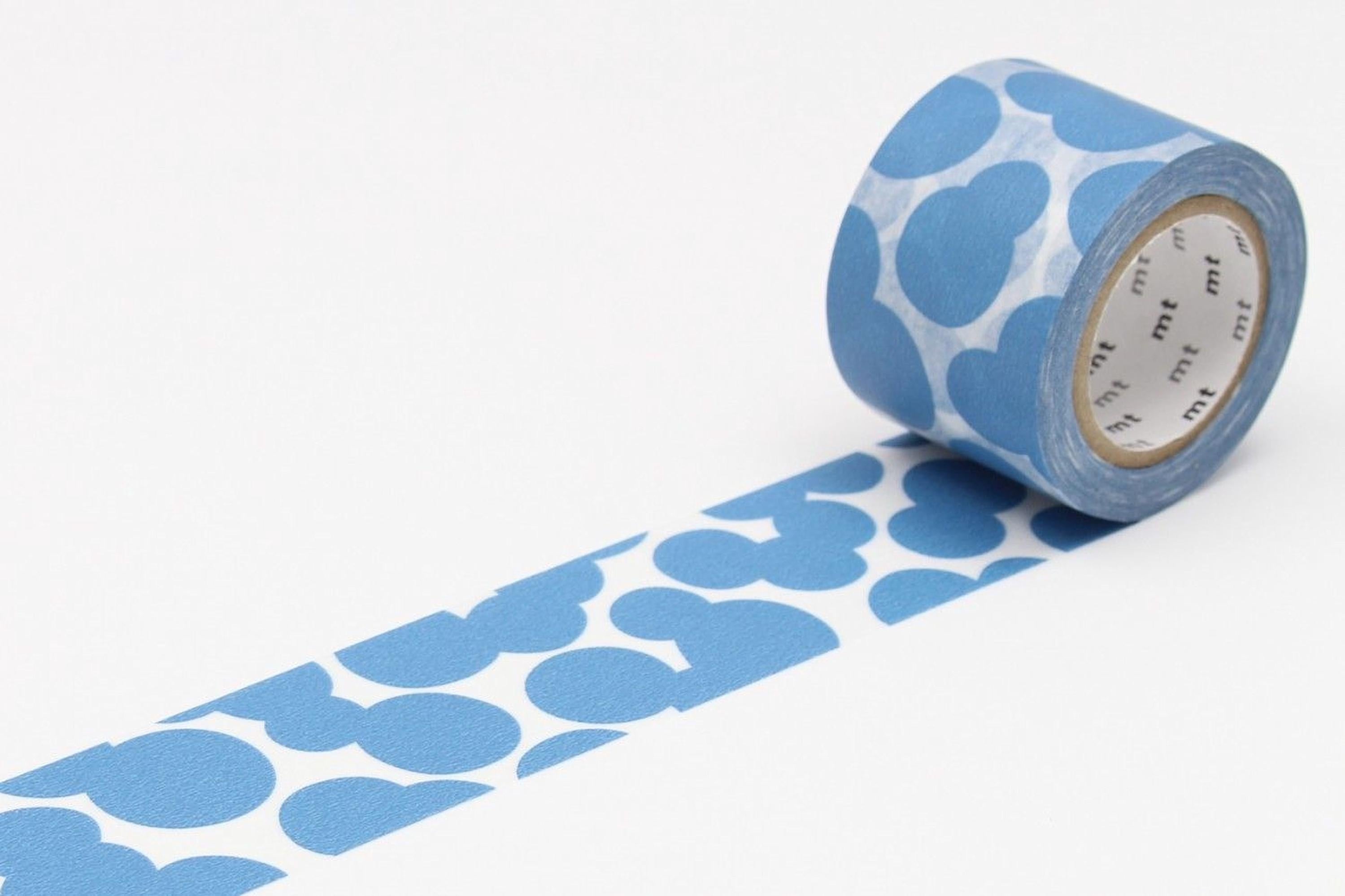 A roll of blue and white patterned tape is lying on a white surface, with the tape partially unwinding and revealing a pattern of blue circles.