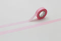 A pink roll of tape is lying on a white surface, with a pink line running across it.