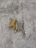 Two small airplane-shaped charms, one gold and one silver, are placed on a gray concrete surface.