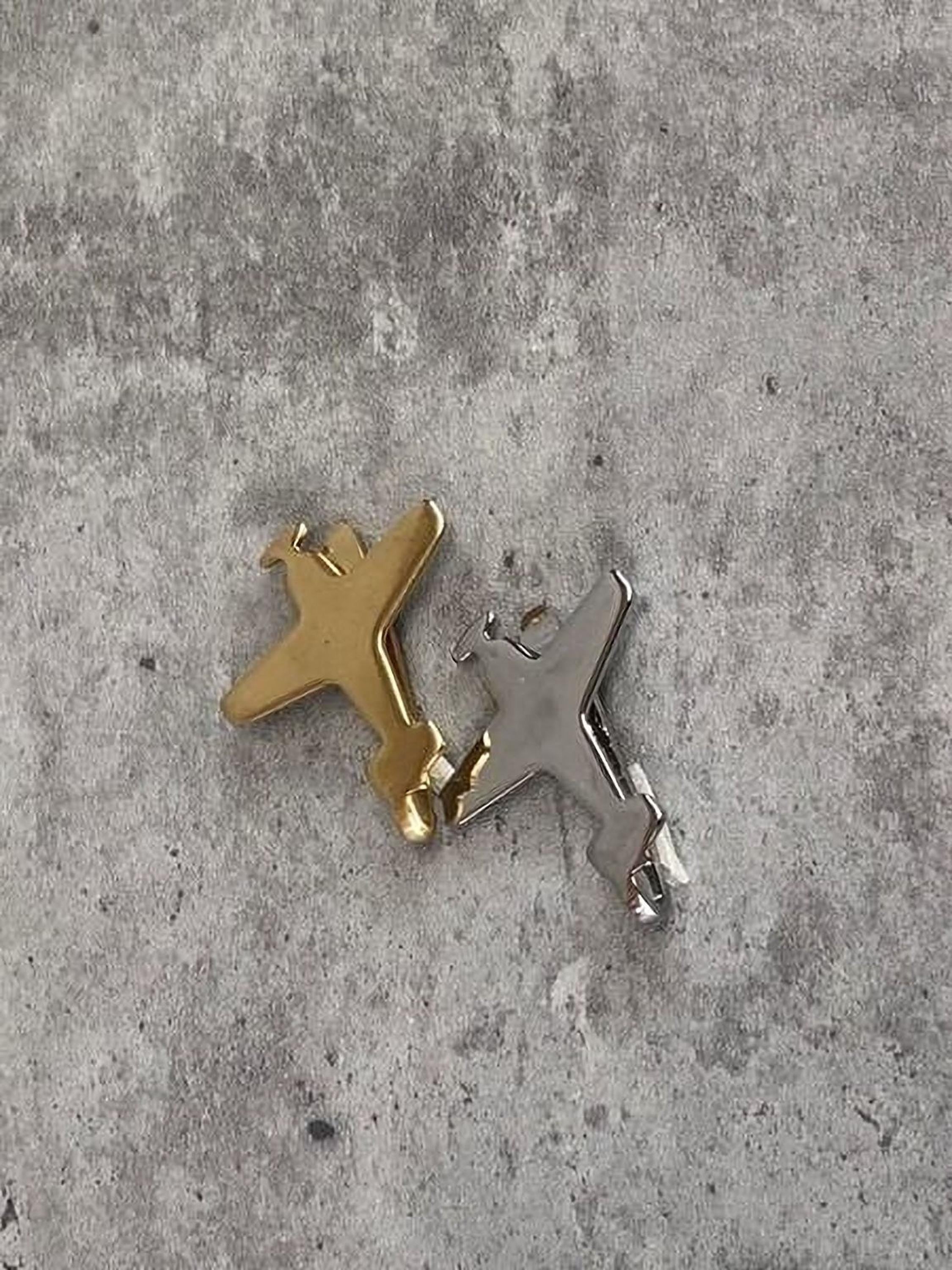 Two small airplane-shaped charms, one gold and one silver, are placed on a gray concrete surface.