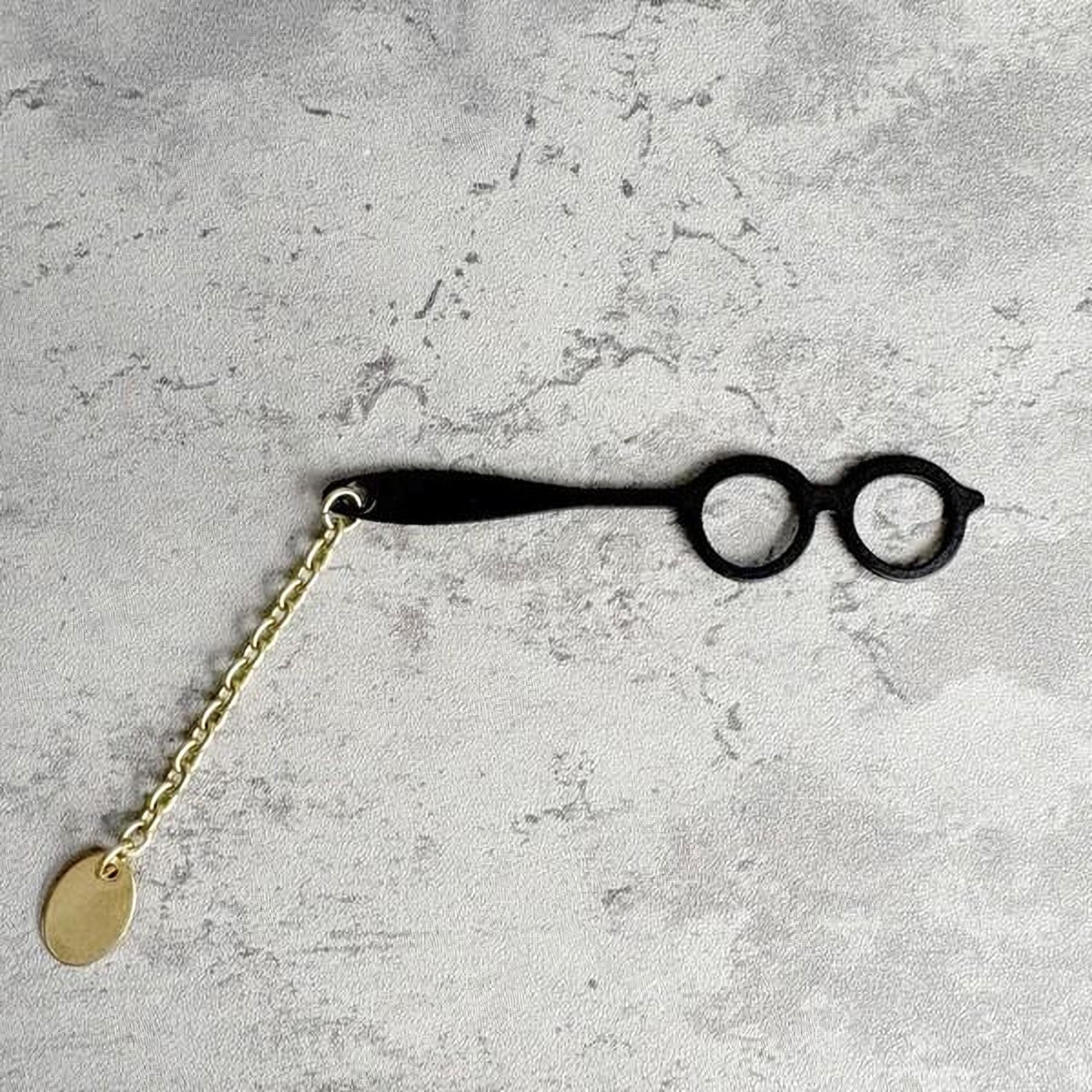 A pair of black glasses with a gold chain attached to the frame, resting on a textured gray surface.