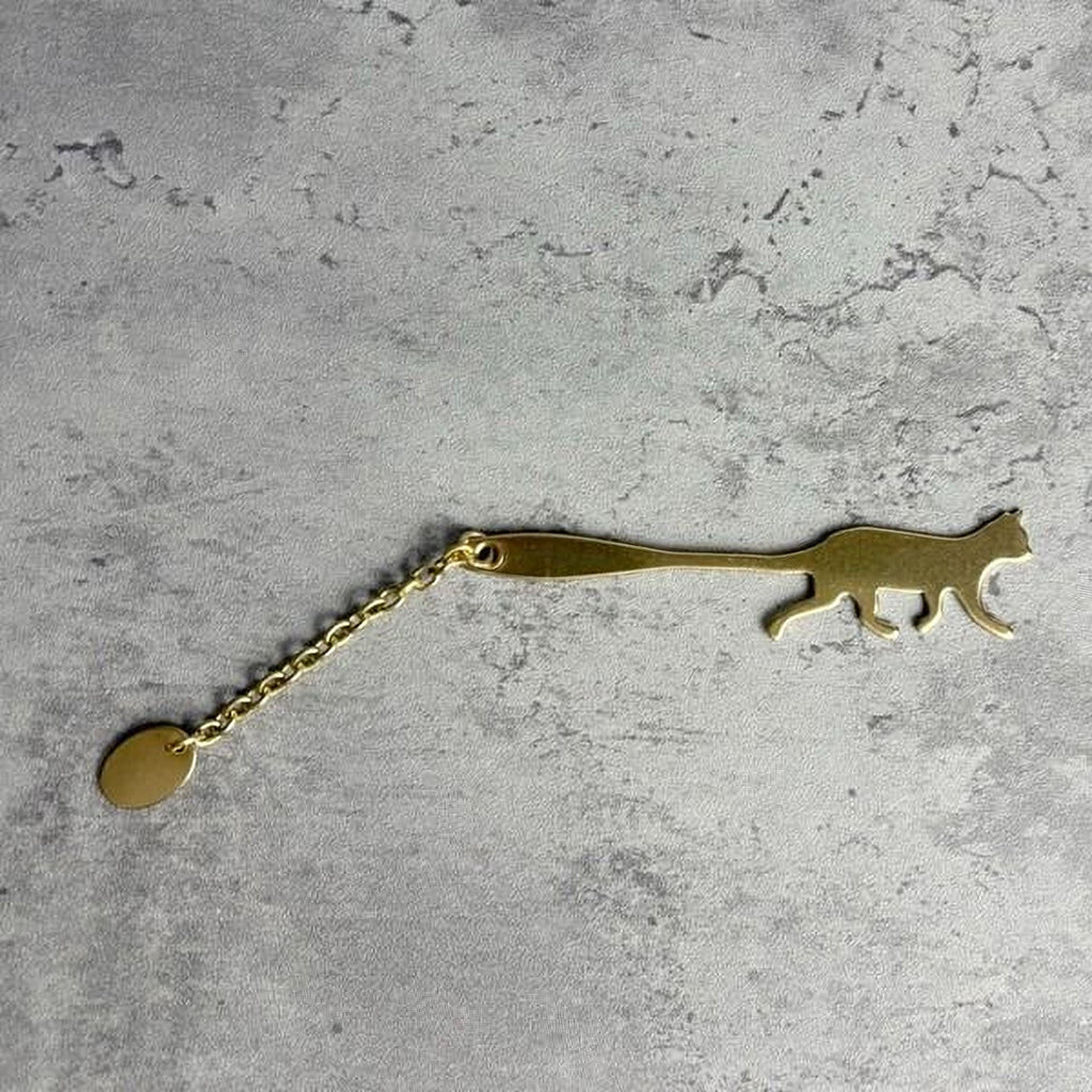 A gold-colored keychain in the shape of a cat is shown on a textured gray surface.
