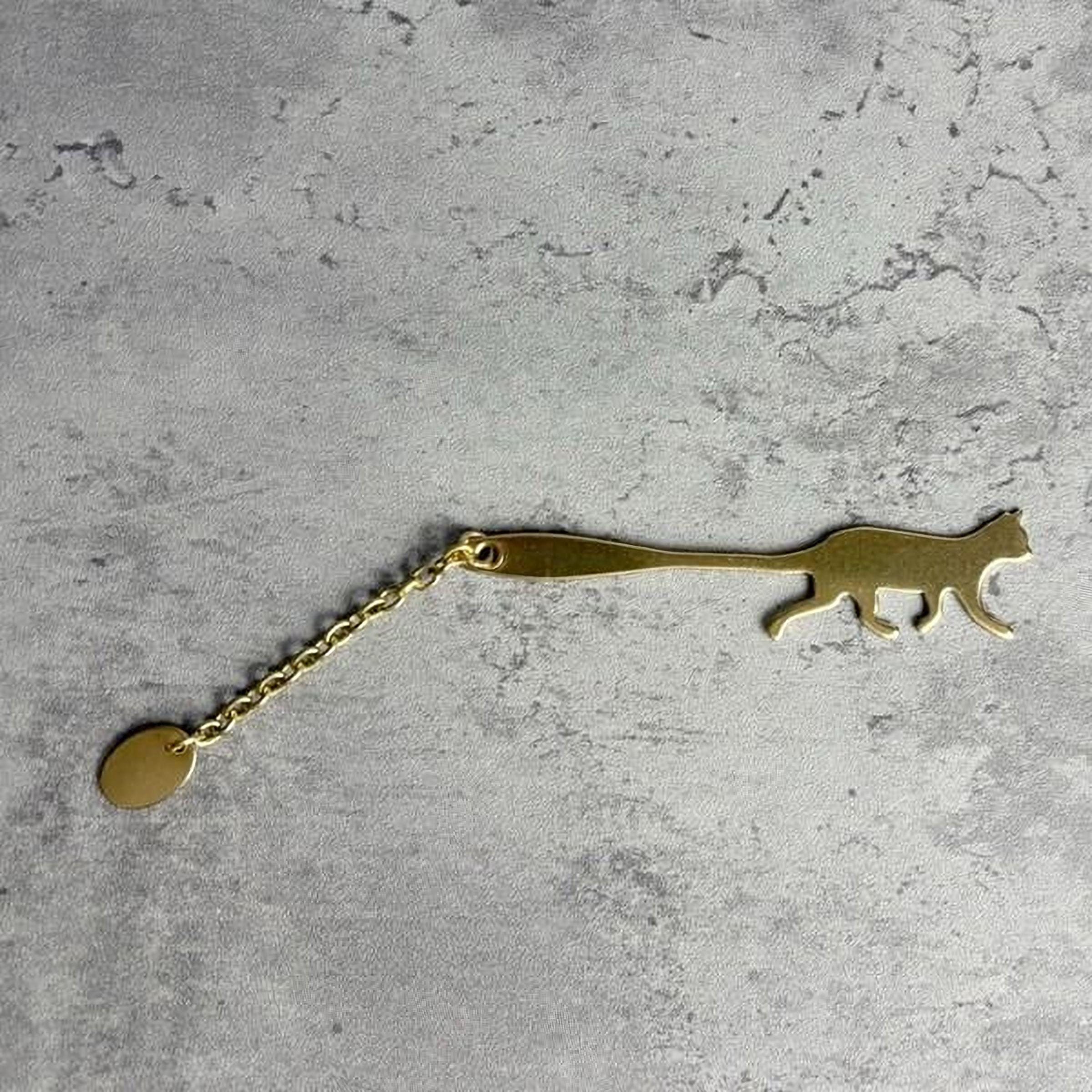 A gold-colored keychain in the shape of a cat is shown on a textured gray surface.