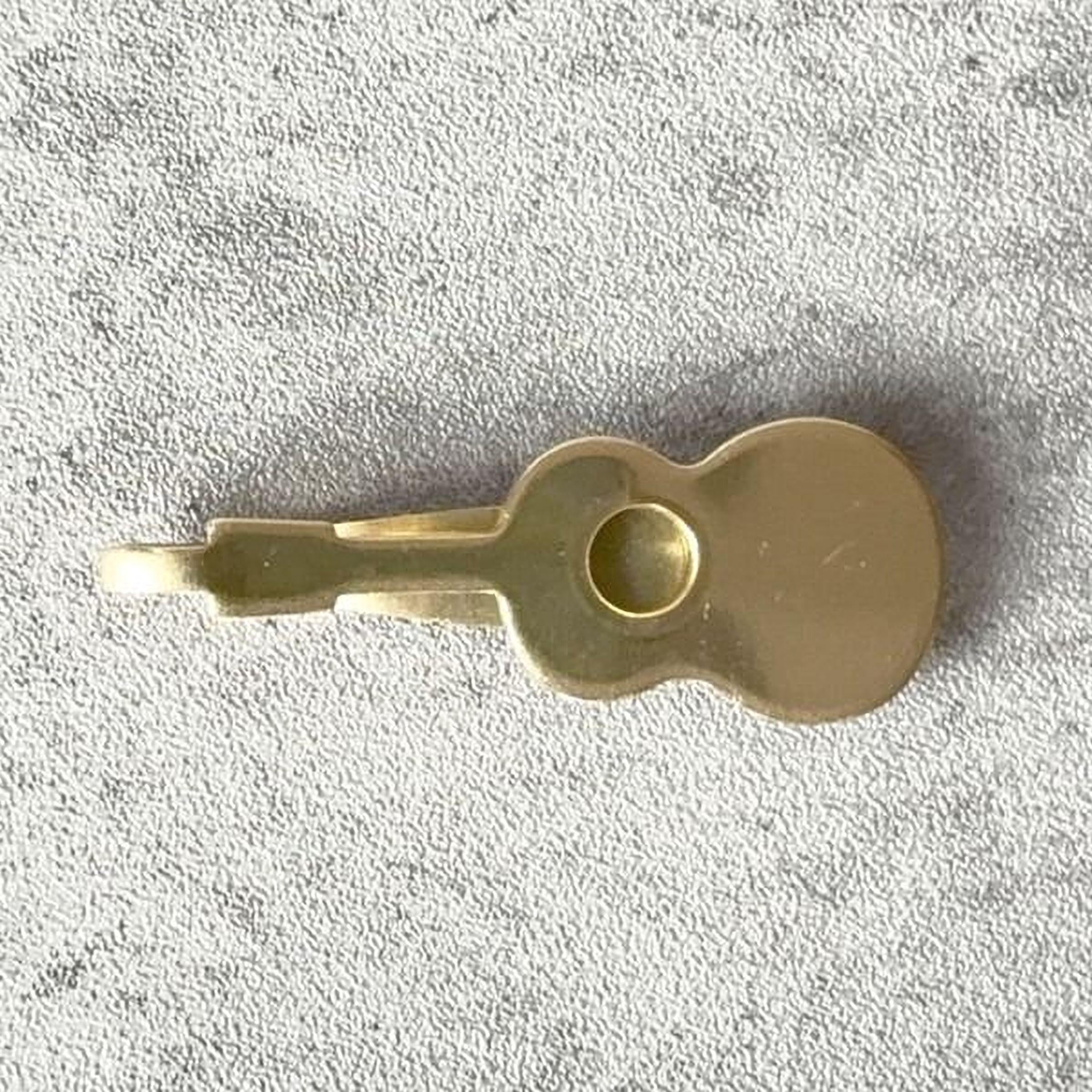 A small golden guitar-shaped keychain is shown on a textured gray surface.