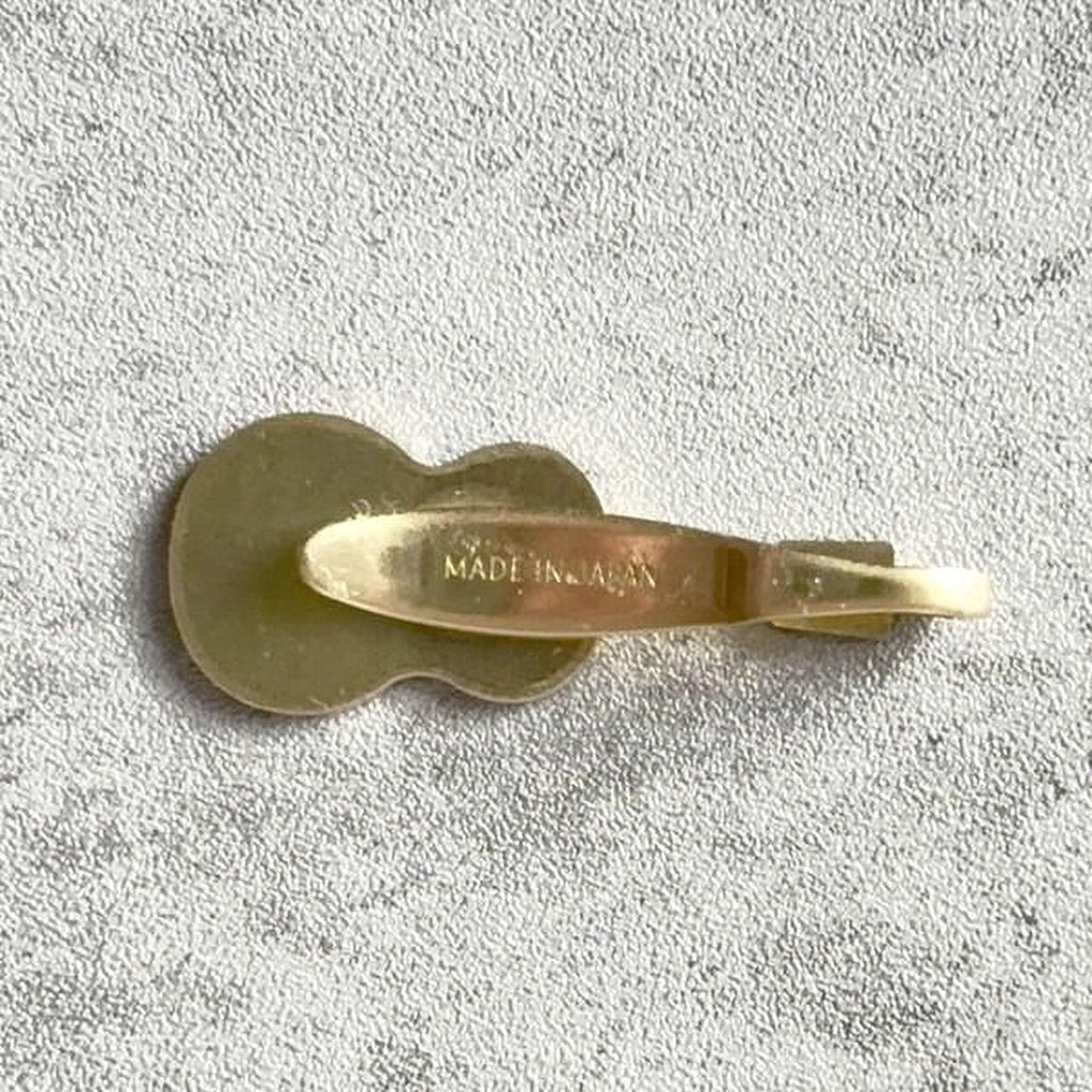 A small gold-colored guitar-shaped object is shown against a textured gray background.