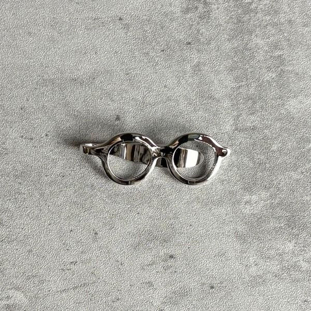 A pair of silver-colored glasses or frames is shown against a textured gray background.