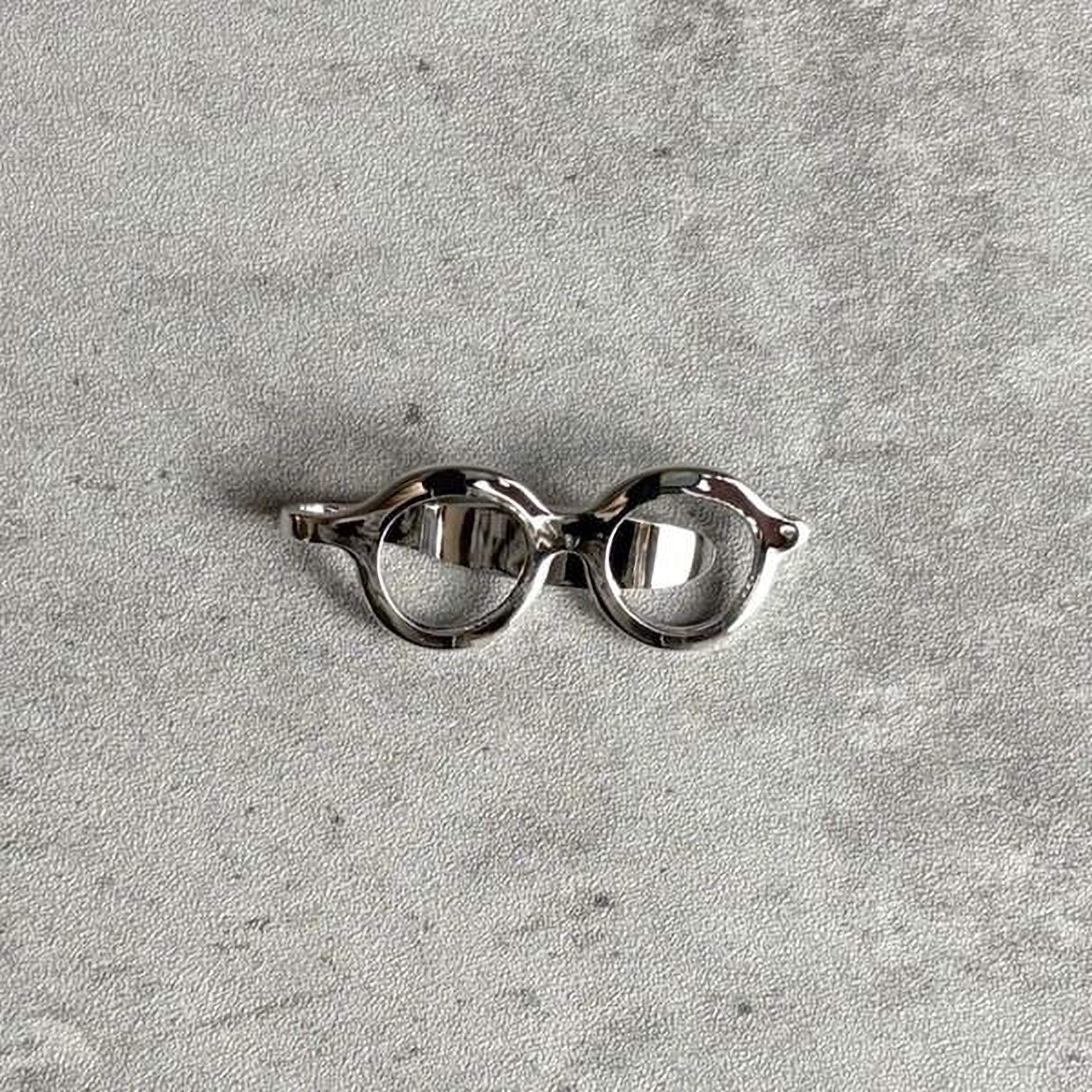 A pair of silver-colored glasses or frames is shown against a textured gray background.