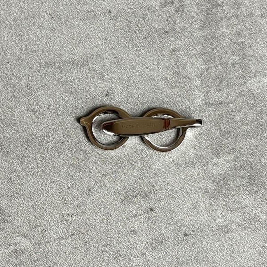 A pair of silver-colored metal scissors with a curved handle, resting on a textured gray surface.