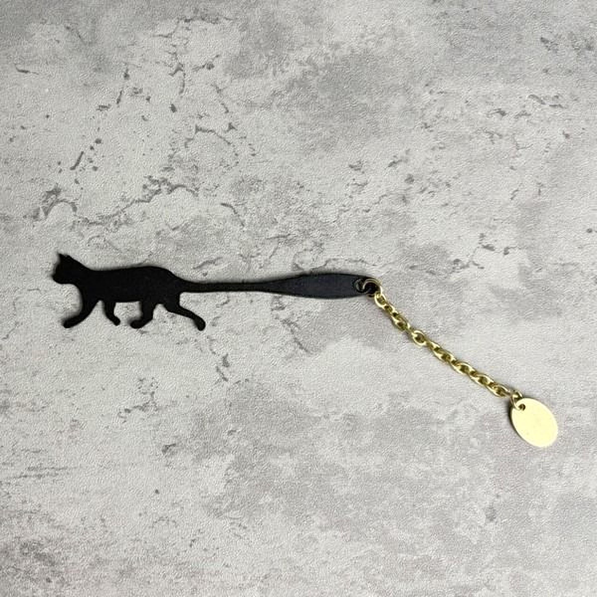 A black silhouette of a cat is shown on a textured gray surface, with a gold chain attached to it.