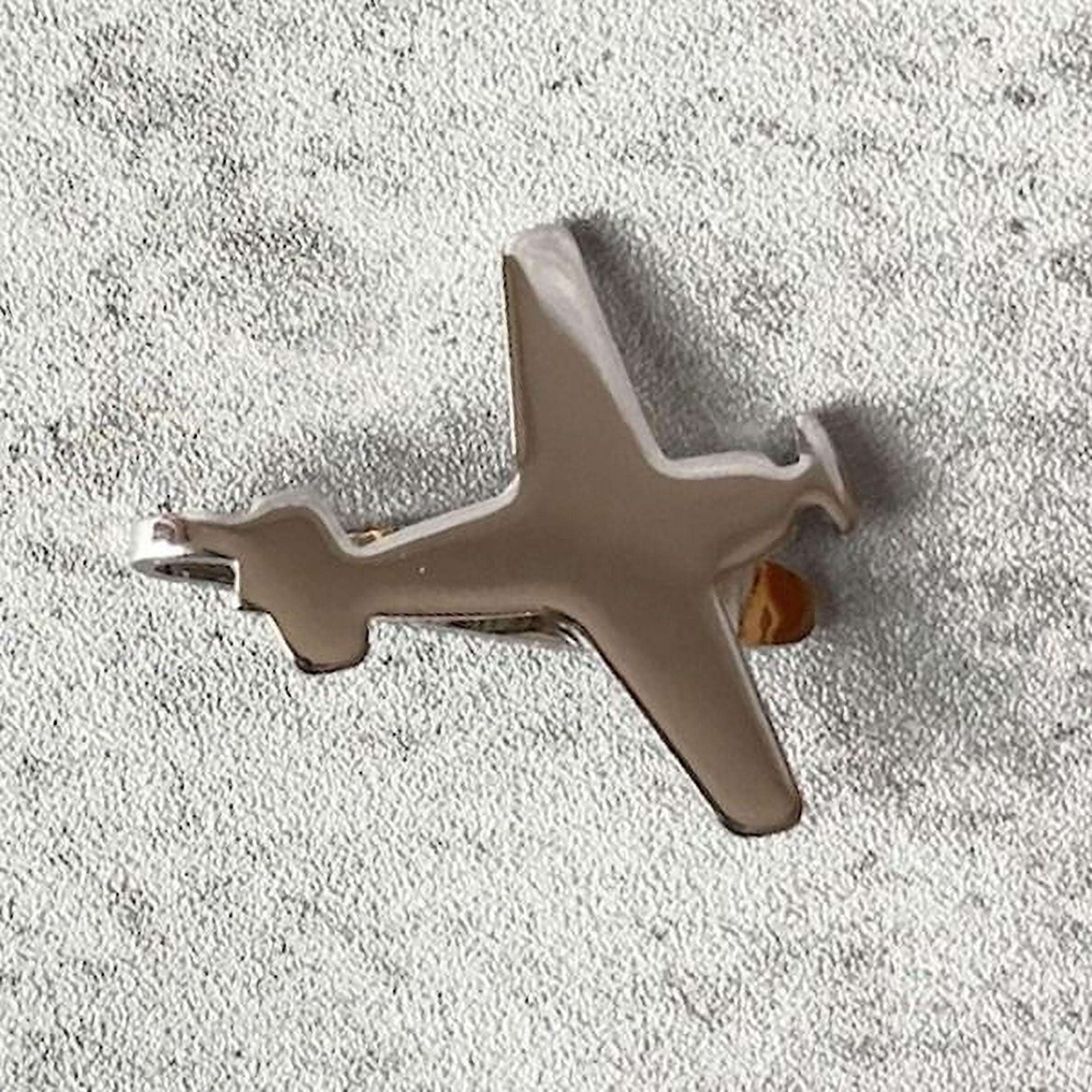 A silver airplane-shaped pendant or brooch is shown against a textured gray background.