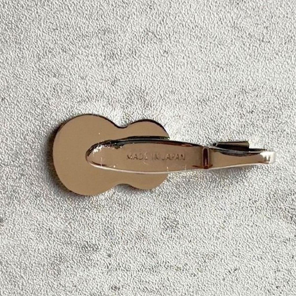 A small, round, metallic object resembling a tie clip or binder clip is shown against a textured, light-colored background.